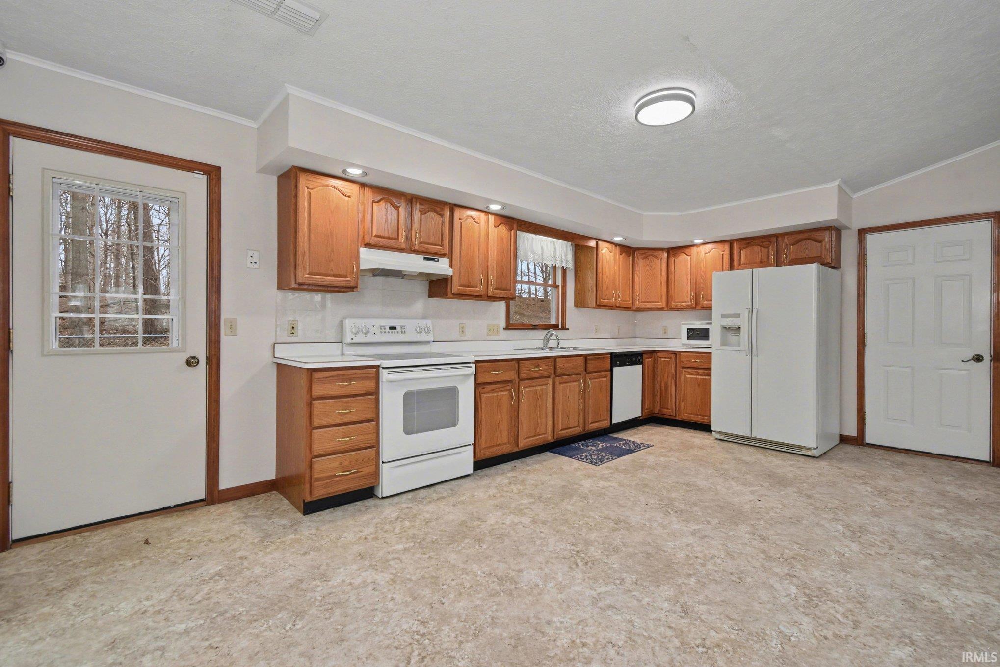 Kitchen featuring white appliances, light countertops, wood finish cabinets, crown molding, and light floors