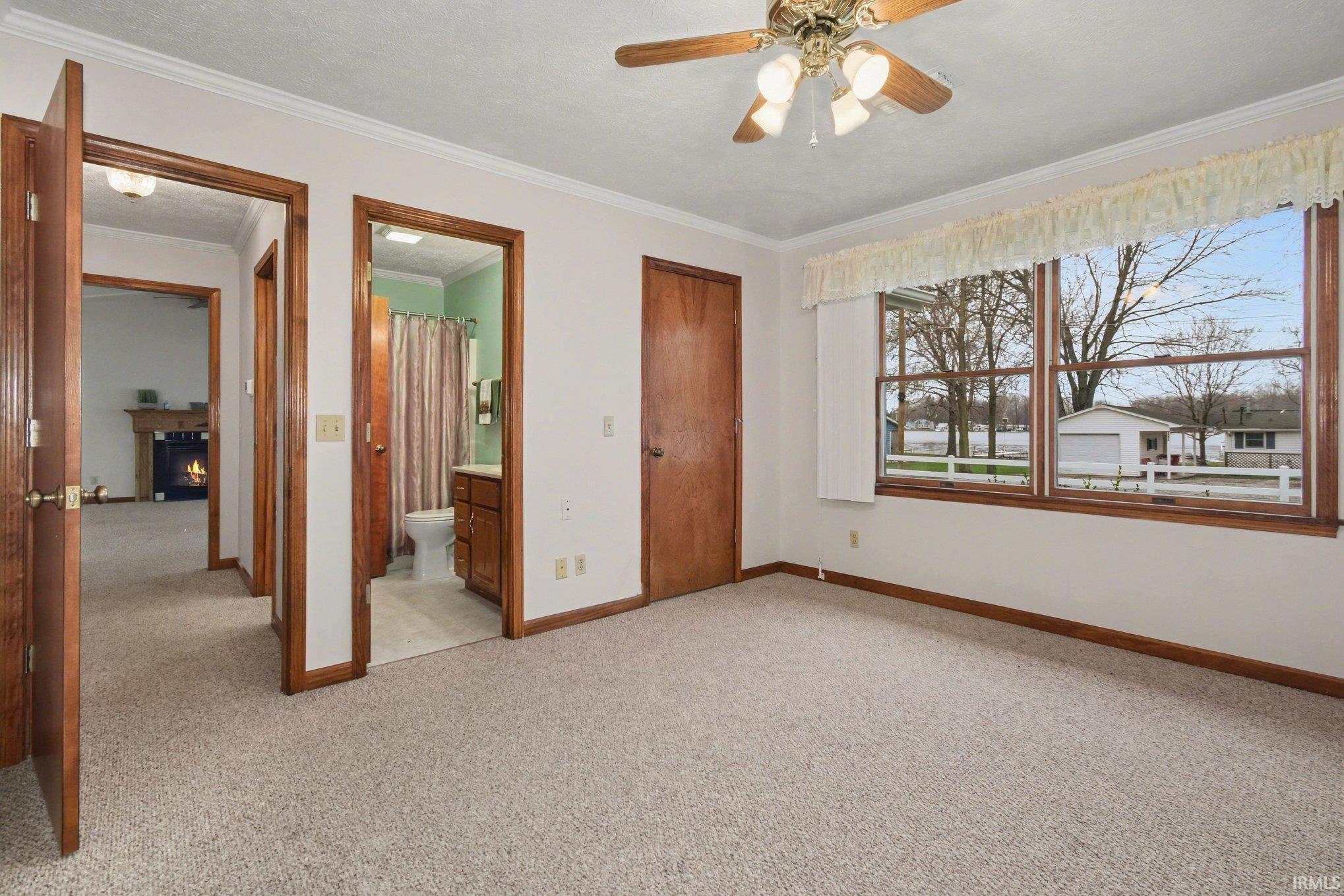 Unfurnished bedroom featuring light colored carpet, ornamental molding, a ceiling fan, ensuite bath, and a closet