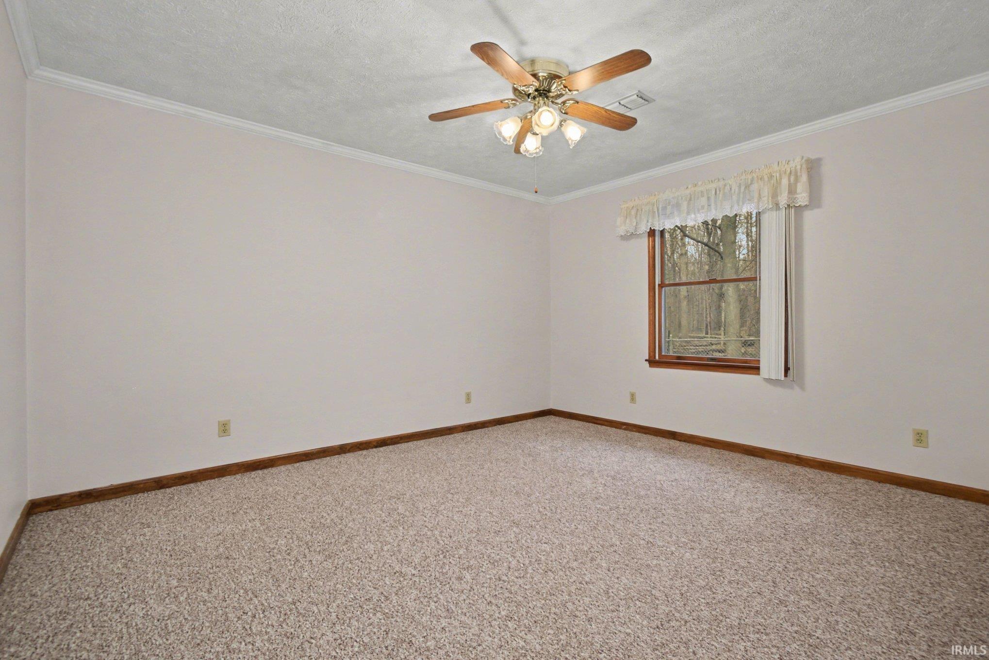 Unfurnished room featuring light colored carpet, crown molding, ceiling fan, and a textured ceiling