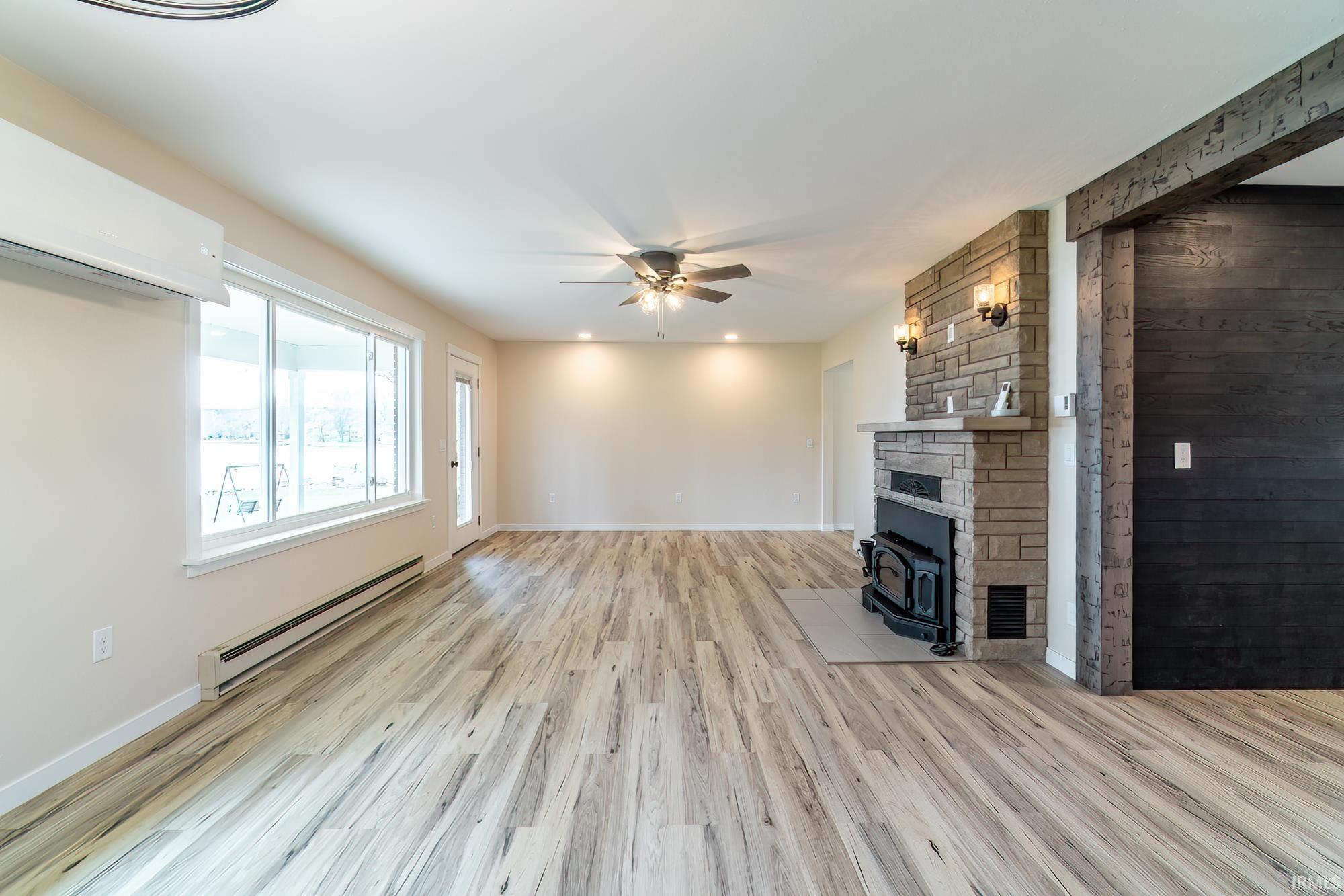 Unfurnished living room featuring a baseboard heating unit, light wood finished floors, ceiling fan, wood walls, and recessed lighting