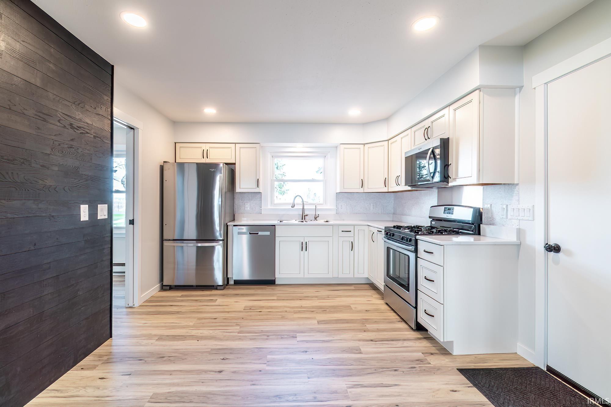 Kitchen with stainless steel appliances, light countertops, light wood-type flooring, backsplash, and white cabinetry