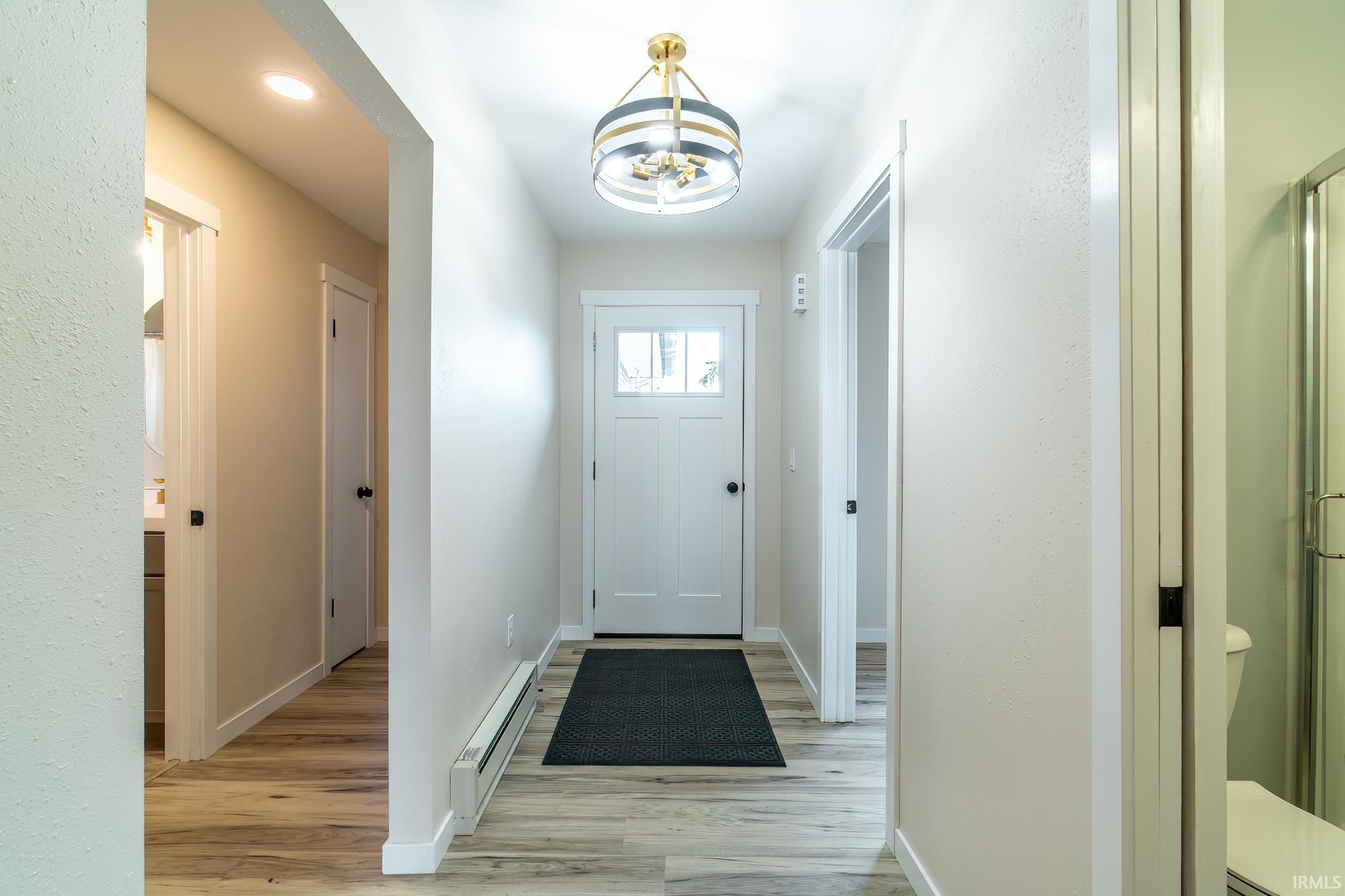 Doorway with hanging lights, a baseboard heating unit, and wood finished floors