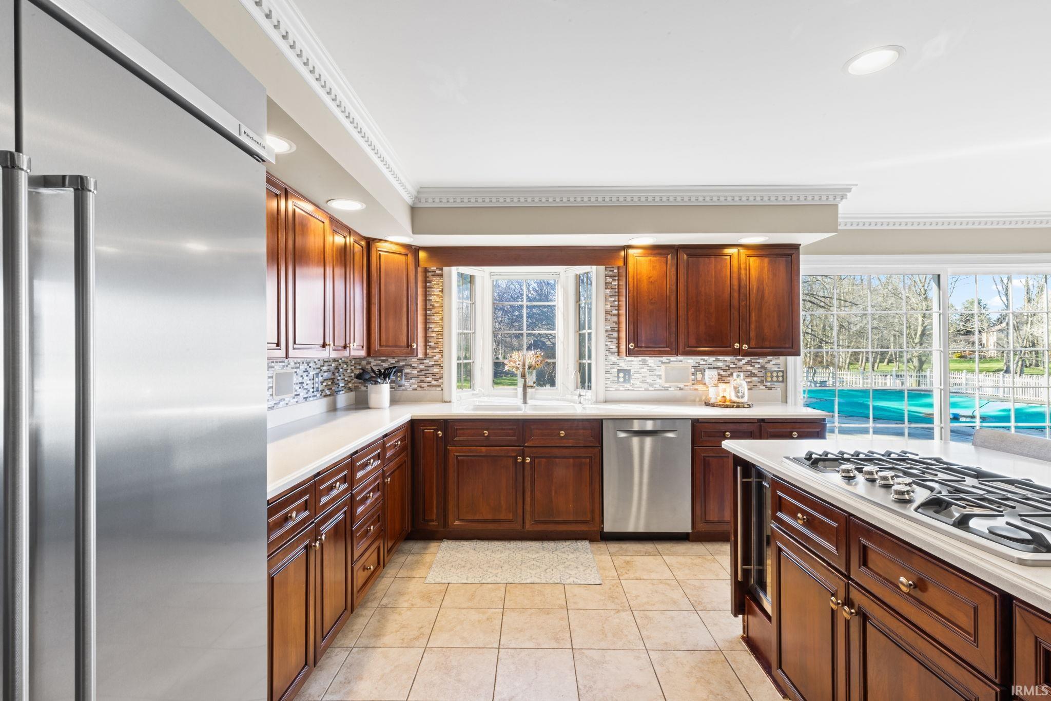 Kitchen with stainless steel appliances, light countertops, ornamental molding, light tile patterned flooring, and healthy amount of natural light