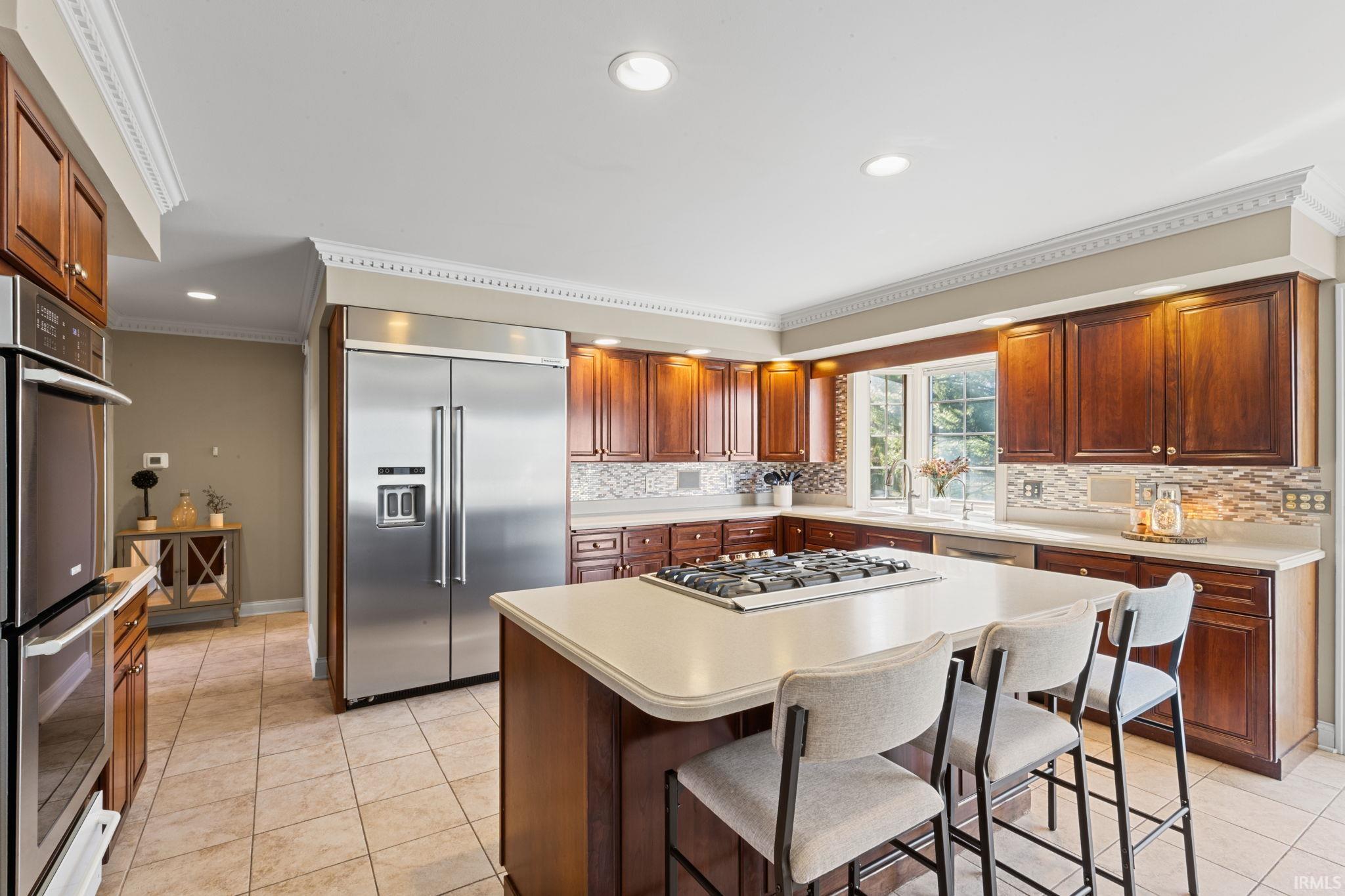 Kitchen featuring crown molding, stainless steel appliances, light countertops, a kitchen breakfast bar, and a kitchen island