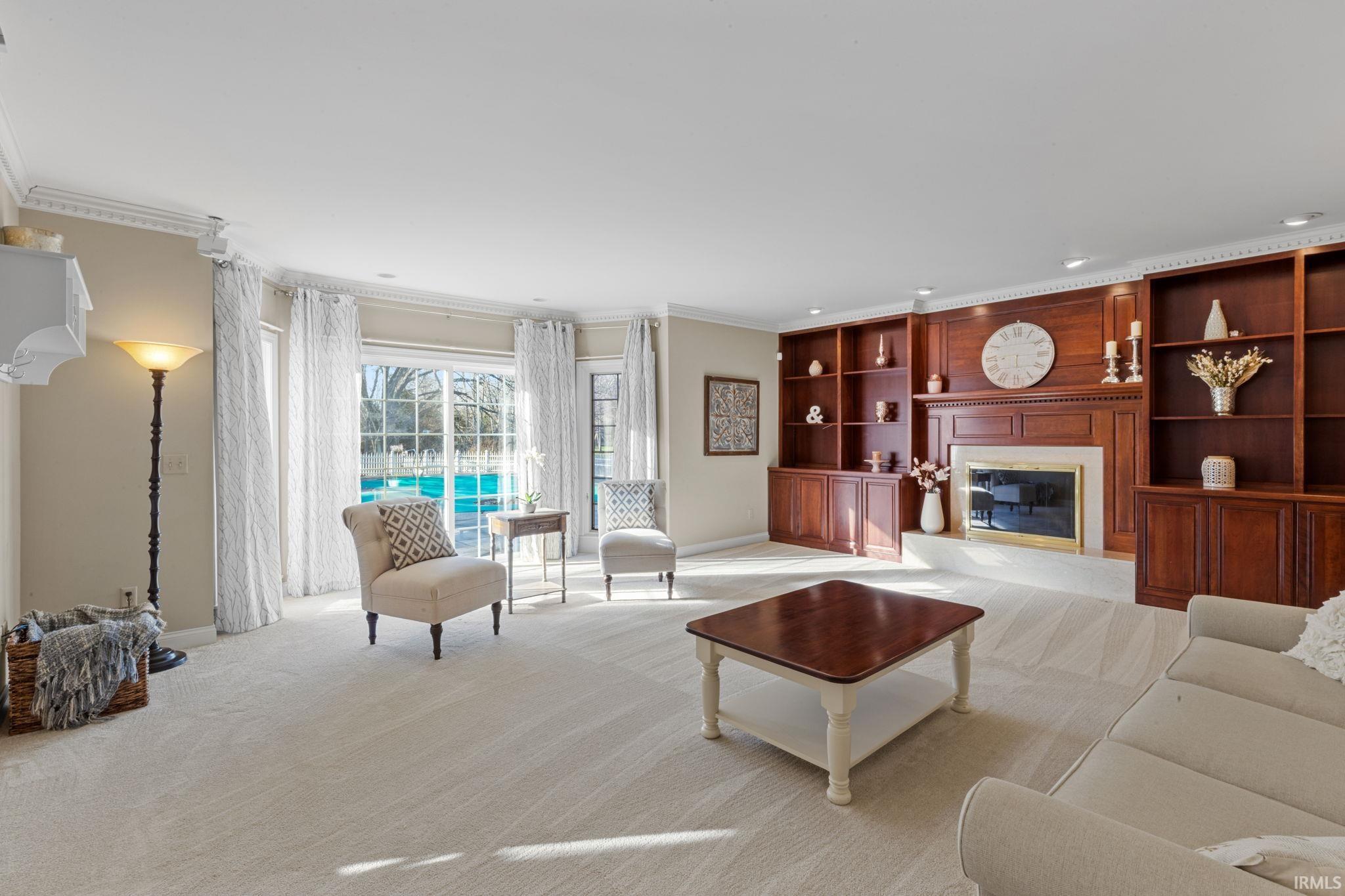 Living room with ornamental molding, a glass covered fireplace, built in shelves, light carpet, and recessed lighting