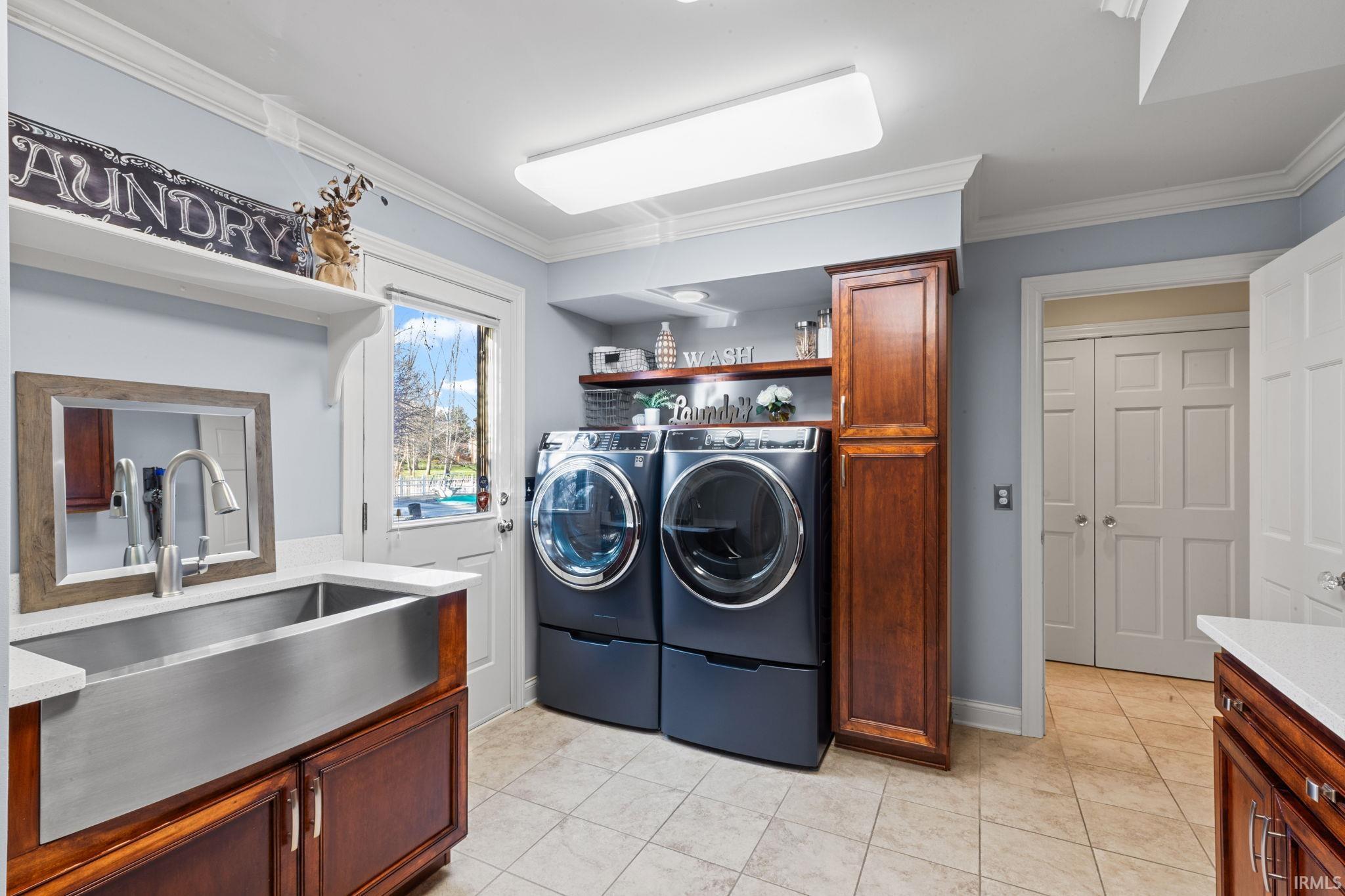 Laundry area featuring crown molding, light tile patterned flooring, washer and clothes dryer, and cabinet space