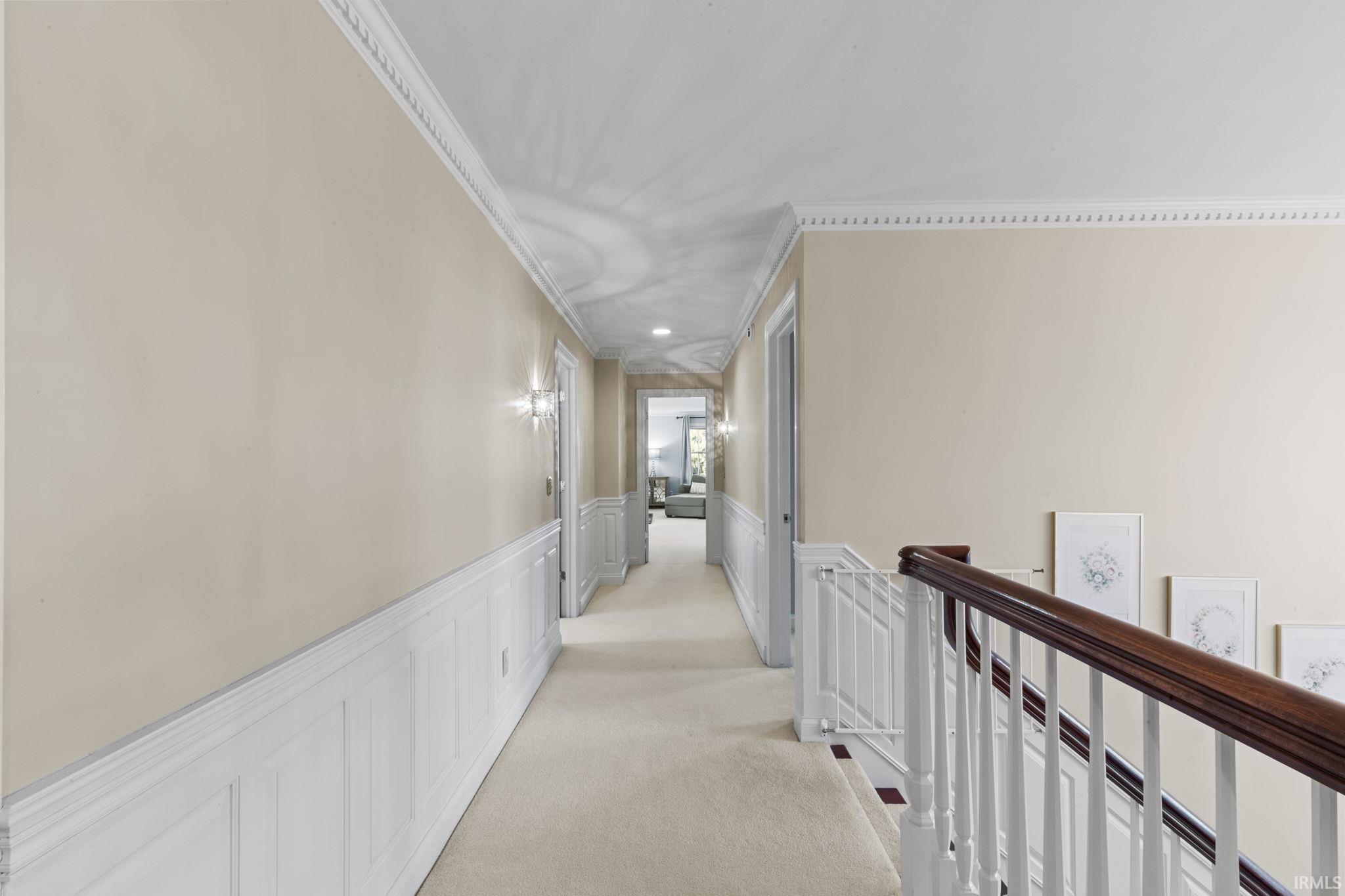 Corridor featuring a wainscoted wall, a decorative wall, crown molding, an upstairs landing, and light carpet