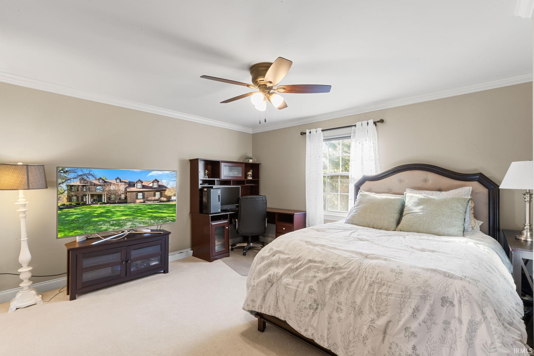 Carpeted bedroom with crown molding, an office area, and a ceiling fan