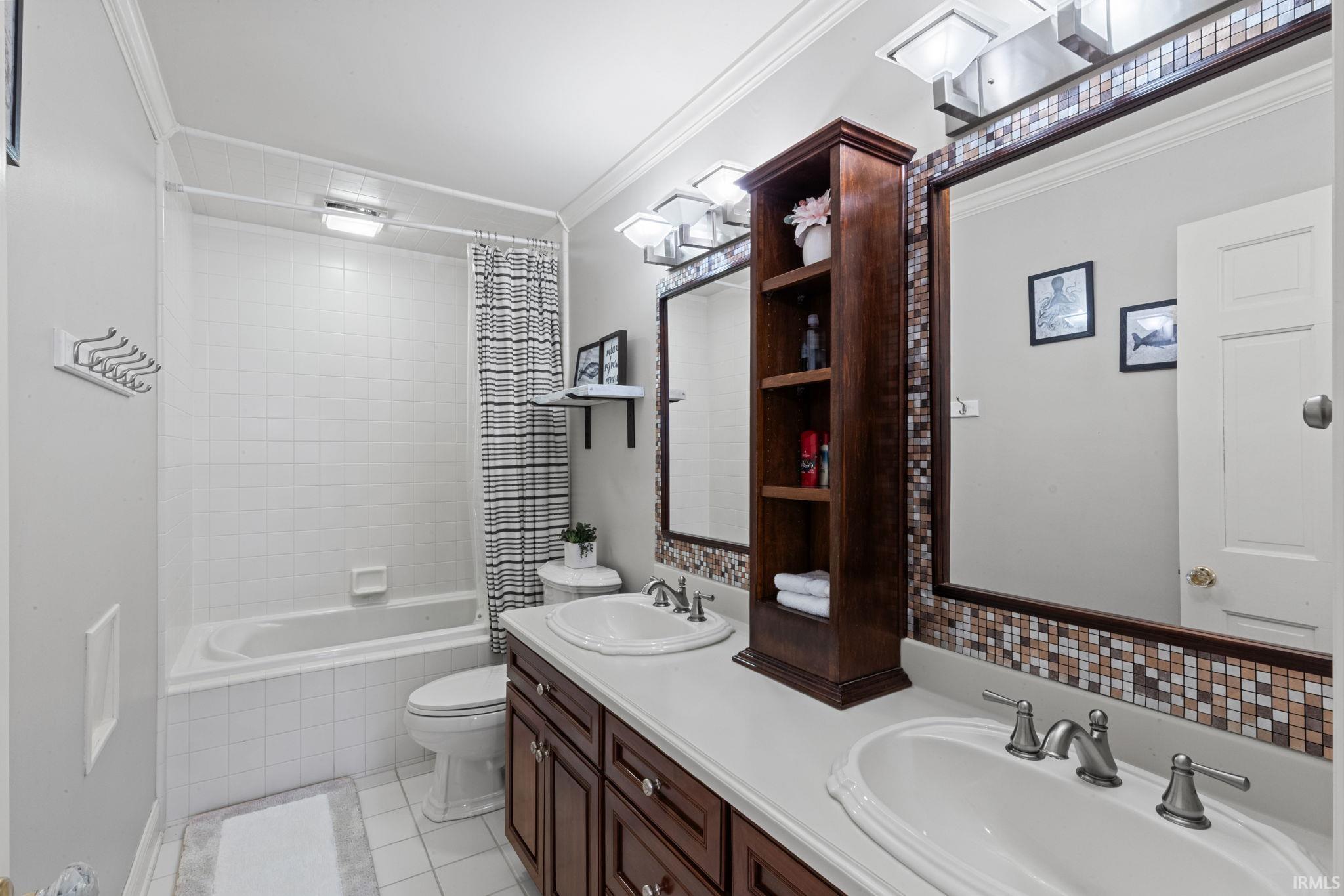 Bathroom featuring ornamental molding, double vanity, tiled shower / bath, and light tile patterned flooring