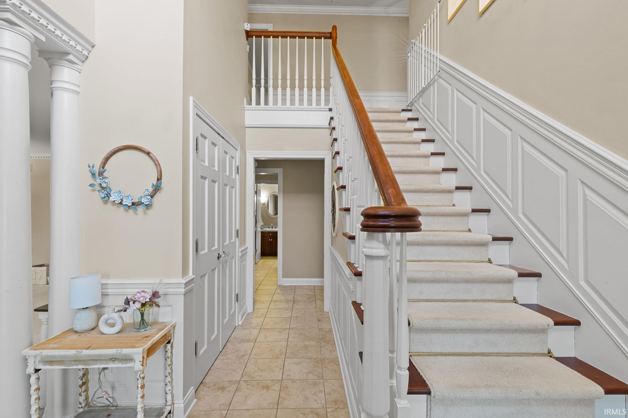 Staircase with wainscoting, a decorative wall, ornamental molding, ornate columns, and tile patterned floors