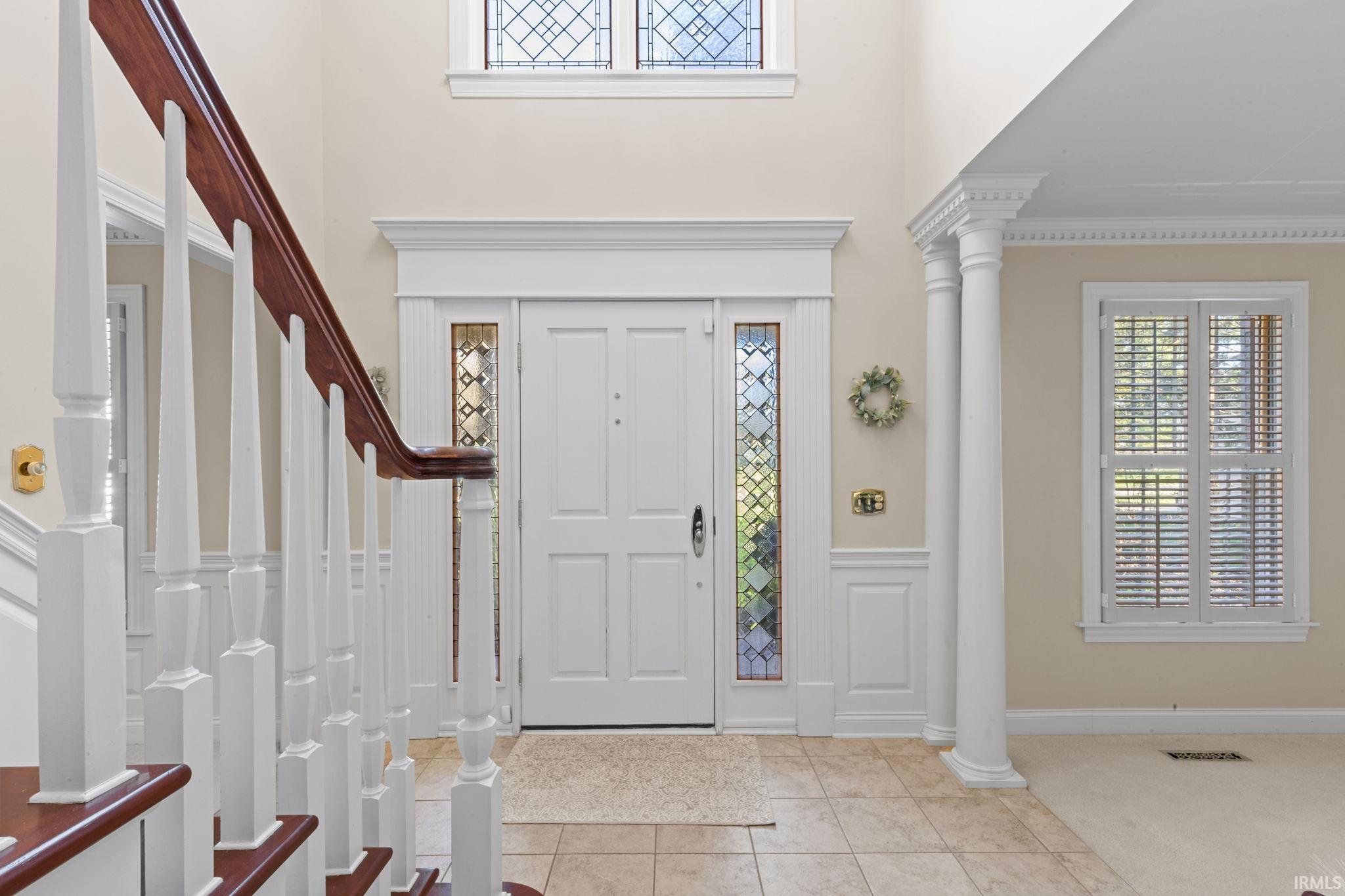 Foyer featuring decorative columns, light tile patterned floors, wainscoting, a high ceiling, and a decorative wall