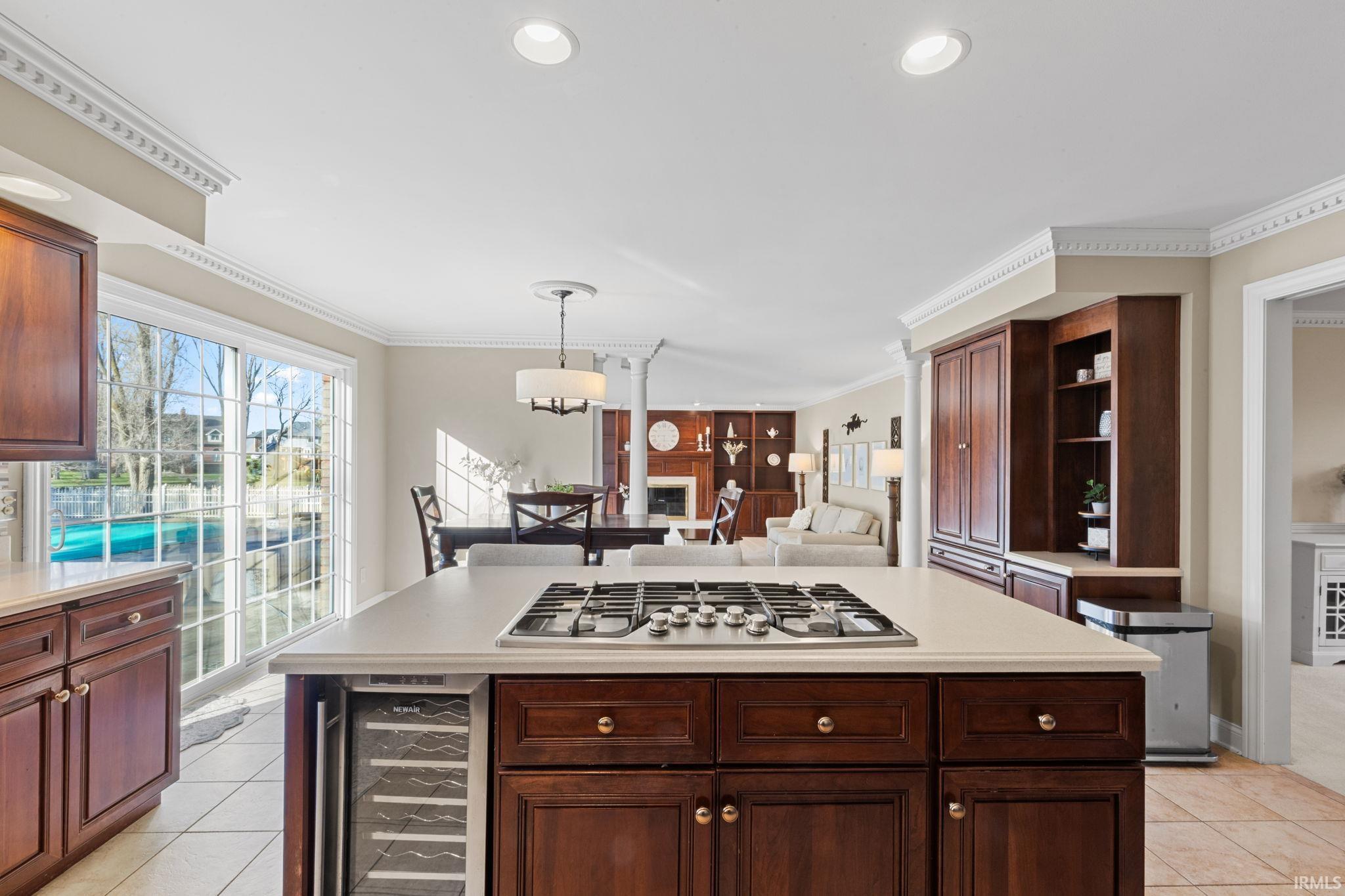 Kitchen featuring a fireplace, crown molding, beverage cooler, decorative light fixtures, and open floor plan