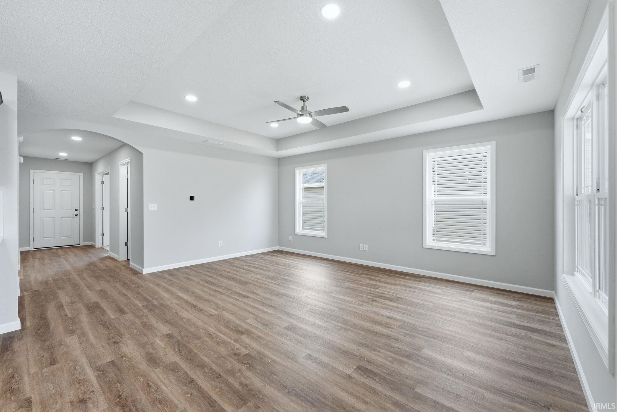 Spare room with arched walkways, ceiling fan, recessed lighting, a tray ceiling, and wood finished floors