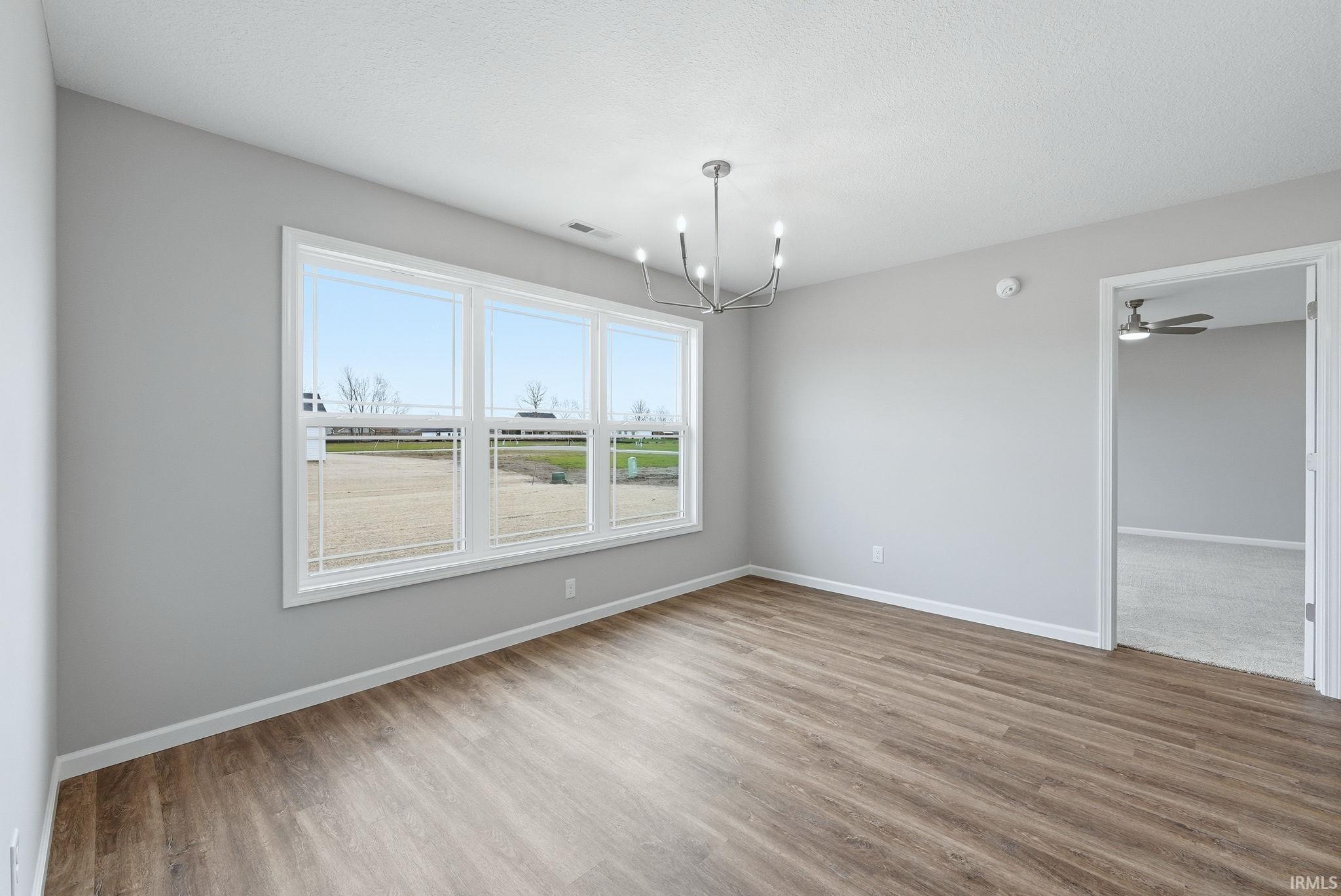 Spare room with light wood finished floors, a chandelier, ceiling fan, and a textured ceiling