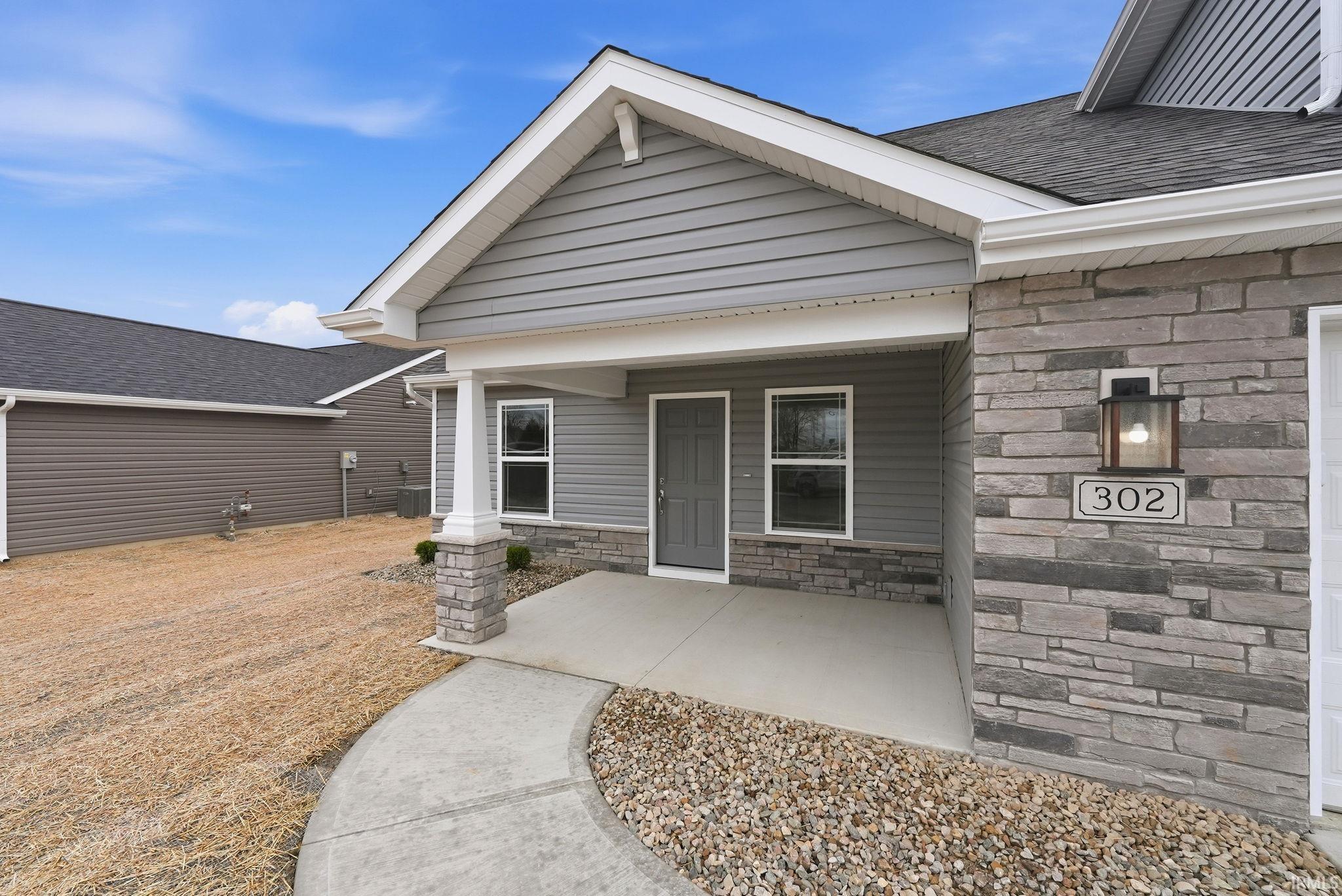 Entrance to property featuring stone siding, covered porch, and roof with shingles