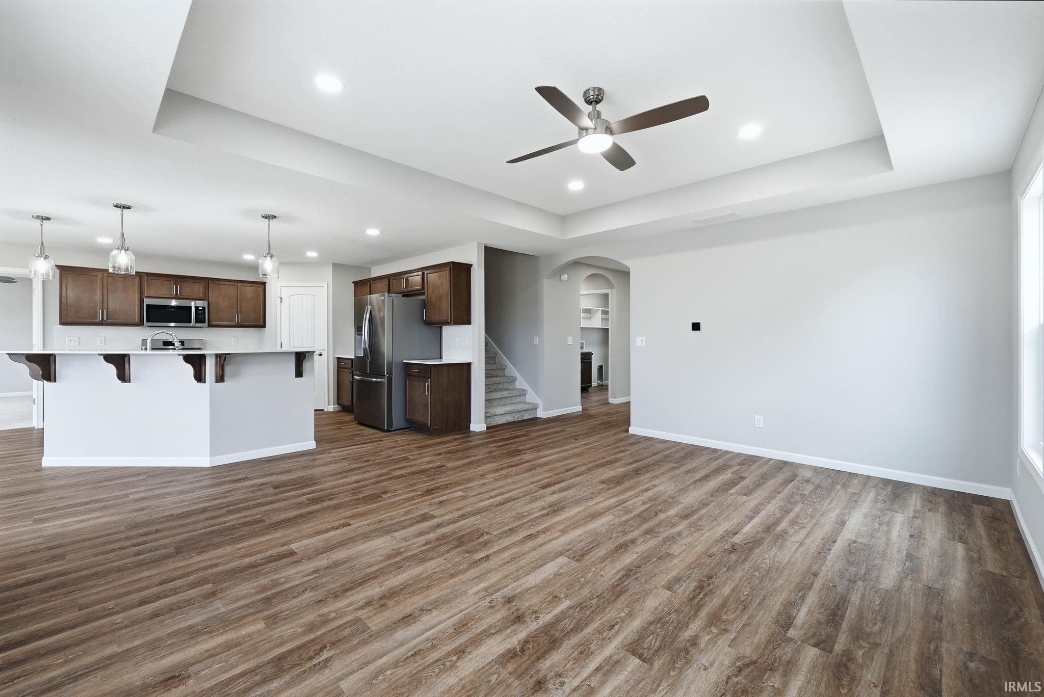 Unfurnished living room featuring arched walkways, dark wood-type flooring, a tray ceiling, ceiling fan, and recessed lighting