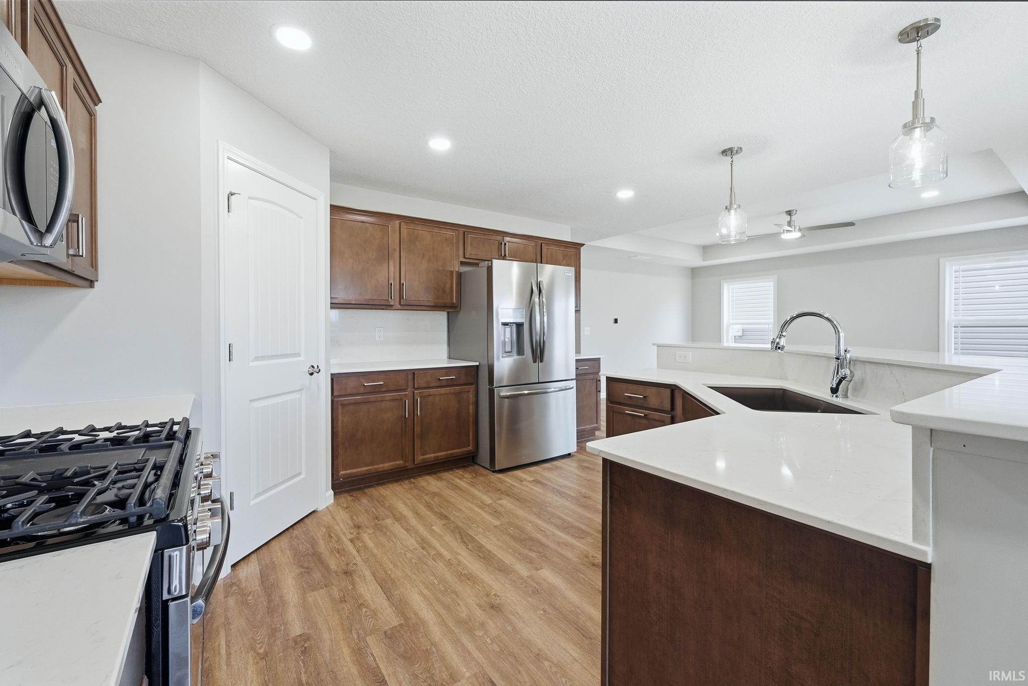 Kitchen with stainless steel appliances, hanging light fixtures, light wood-style flooring, light stone counters, and a raised ceiling