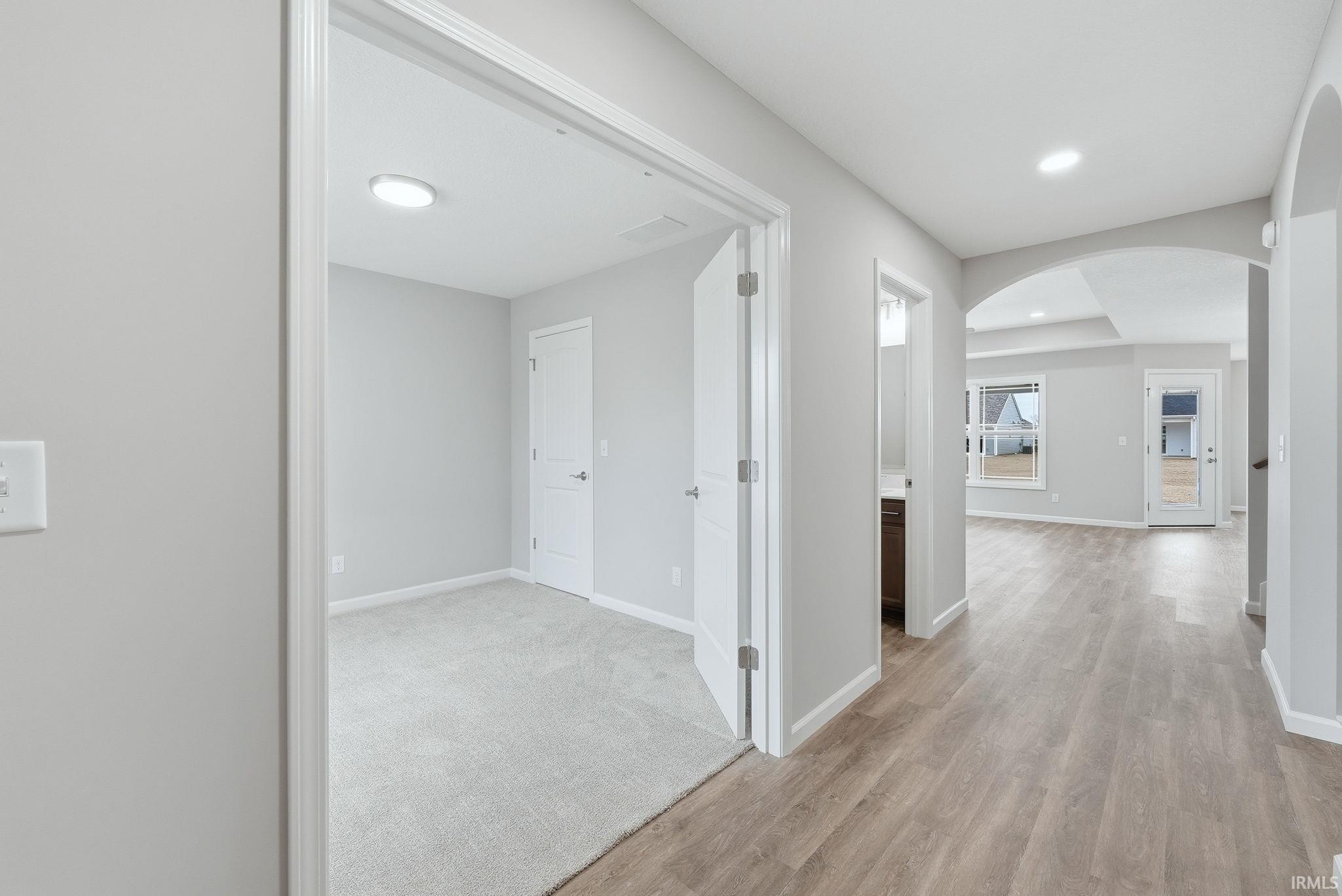 Hallway with arched walkways, light wood-style floors, and recessed lighting