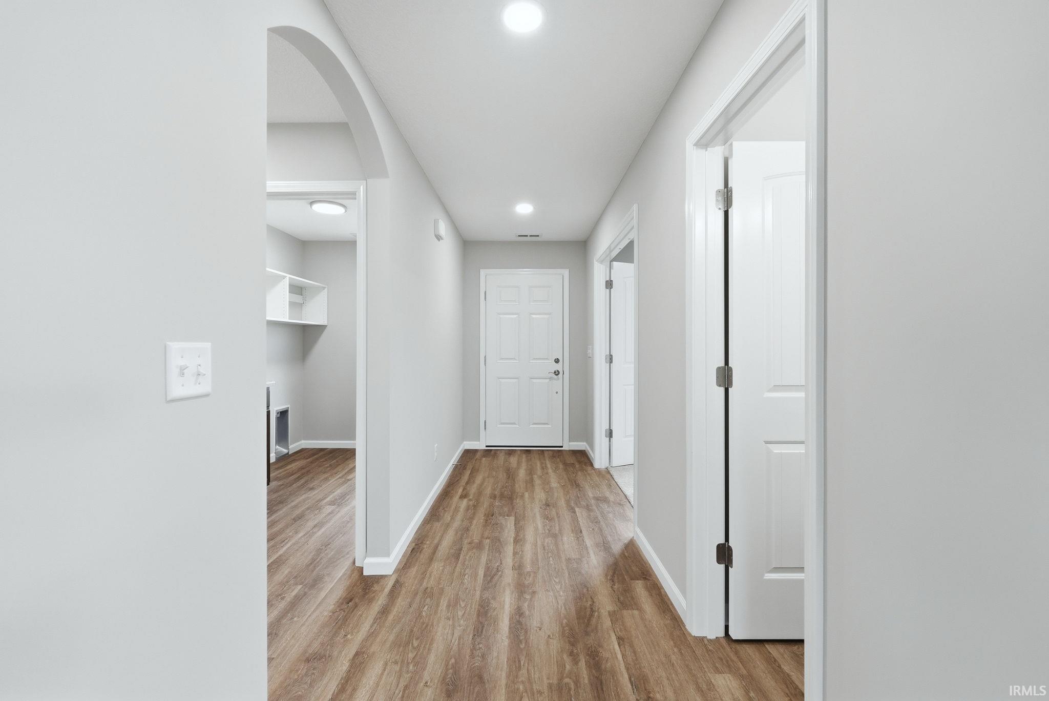 Hallway with light wood-style flooring, recessed lighting, and arched walkways
