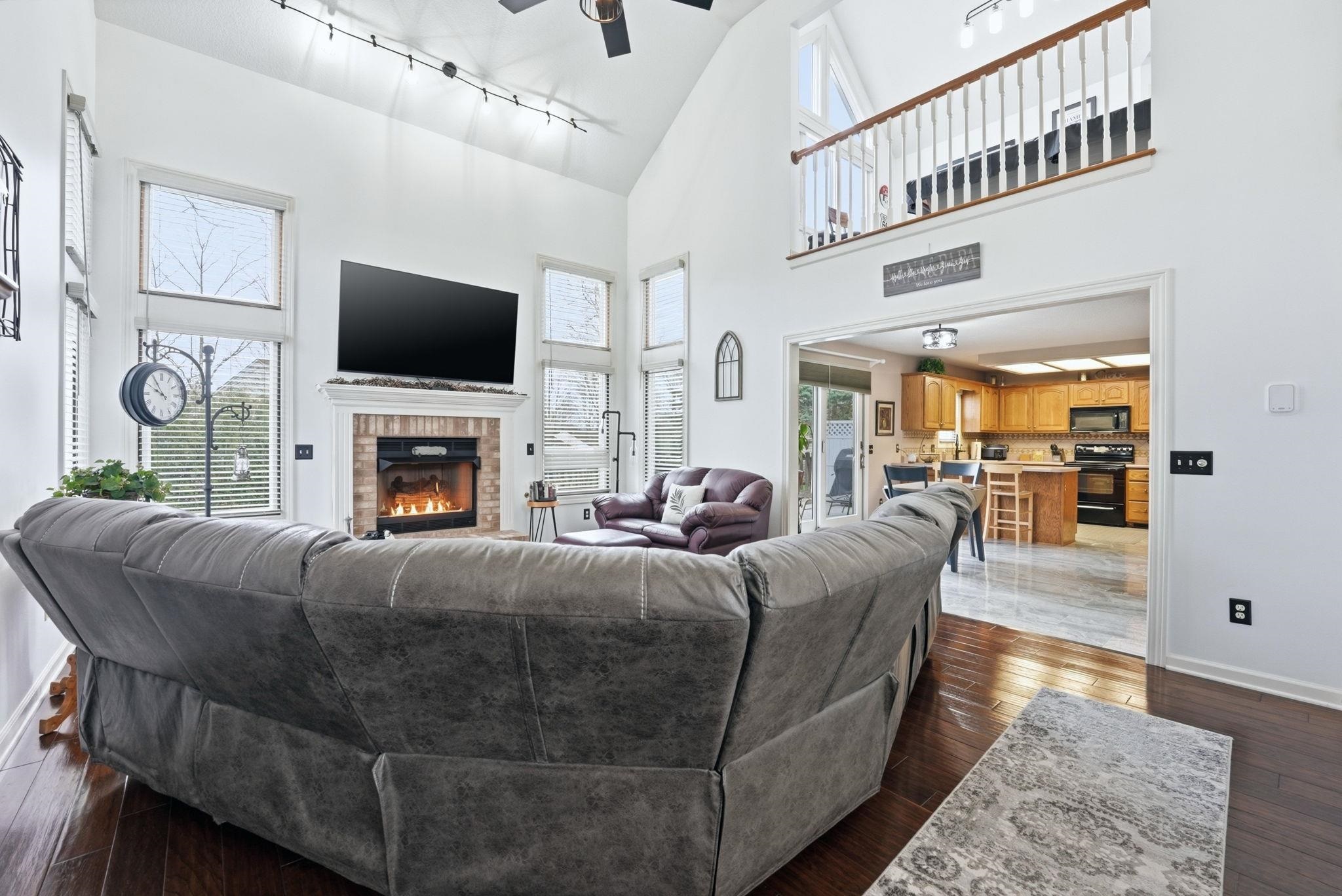 Living area featuring a ceiling fan, rail lighting, dark wood-type flooring, a brick fireplace, and vaulted ceiling