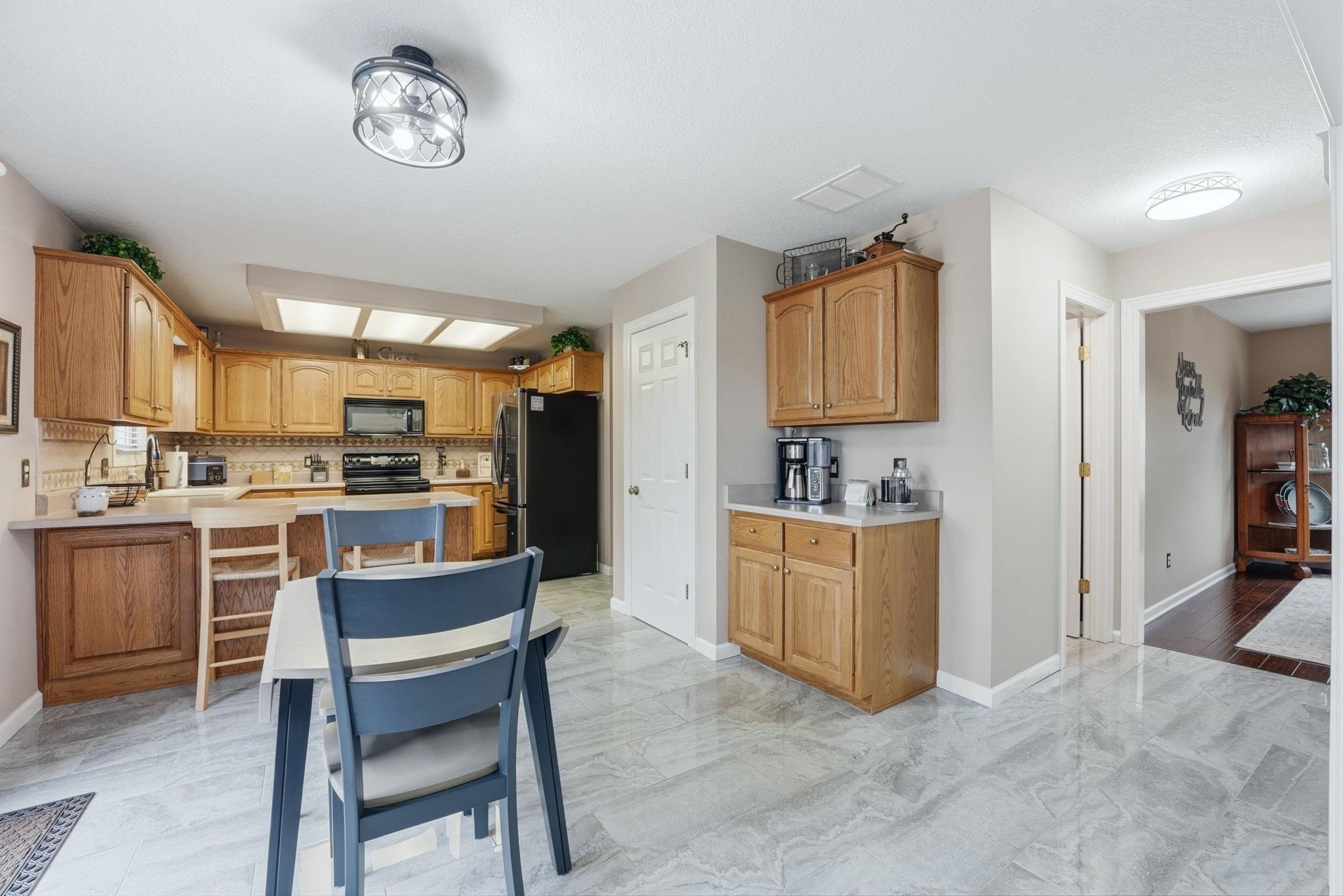 Kitchen with light countertops, black appliances, a peninsula, wood finish cabinetry, and tasteful backsplash
