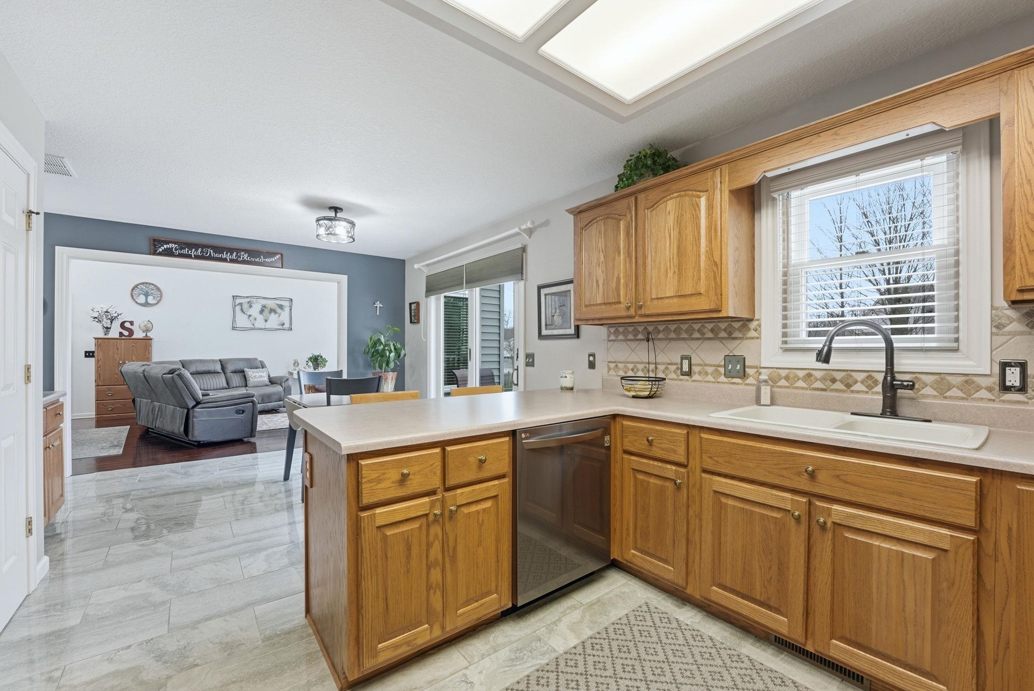 Kitchen with light countertops, backsplash, a peninsula, and stainless steel dishwasher