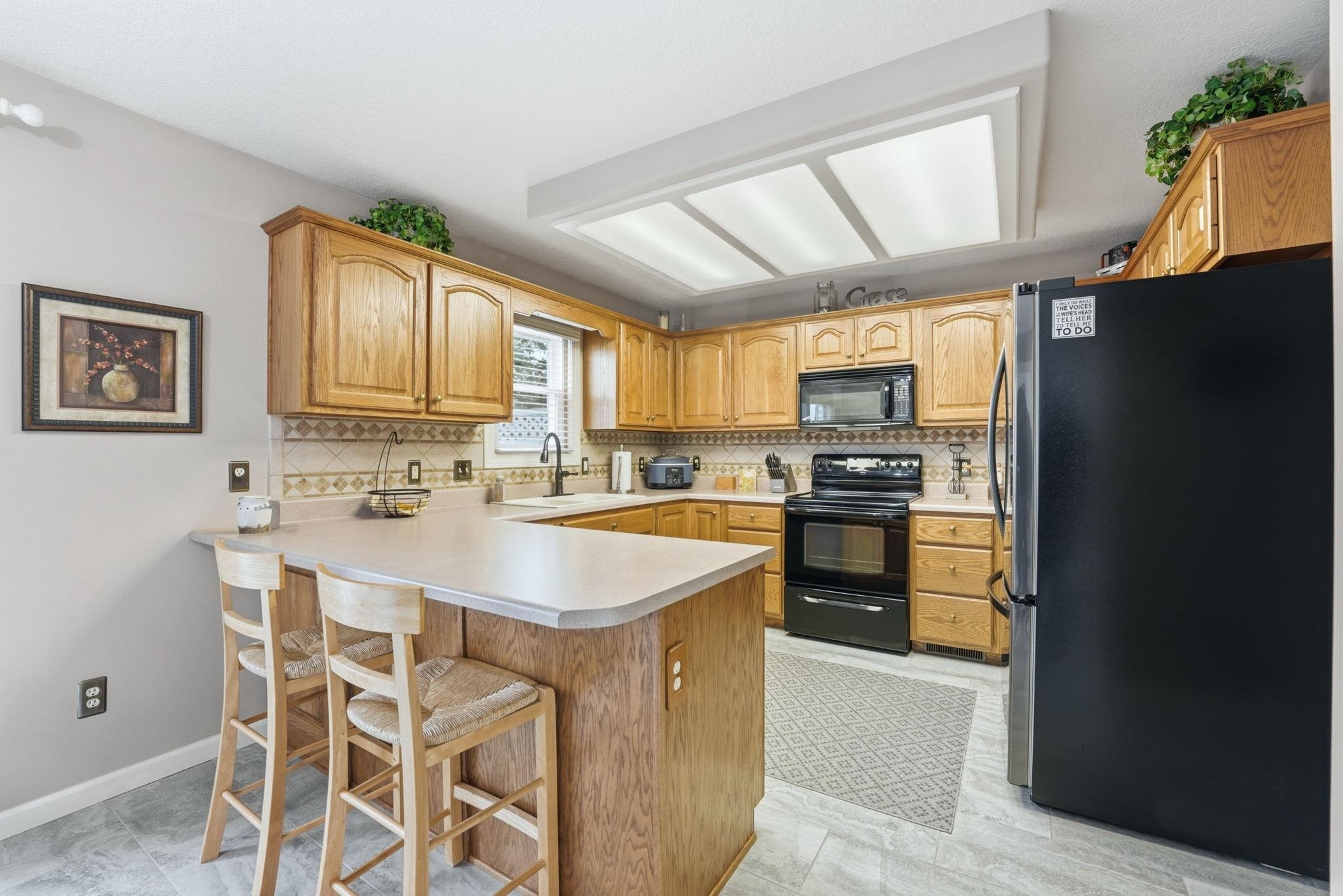 Kitchen featuring black appliances, a peninsula, a kitchen bar, and backsplash