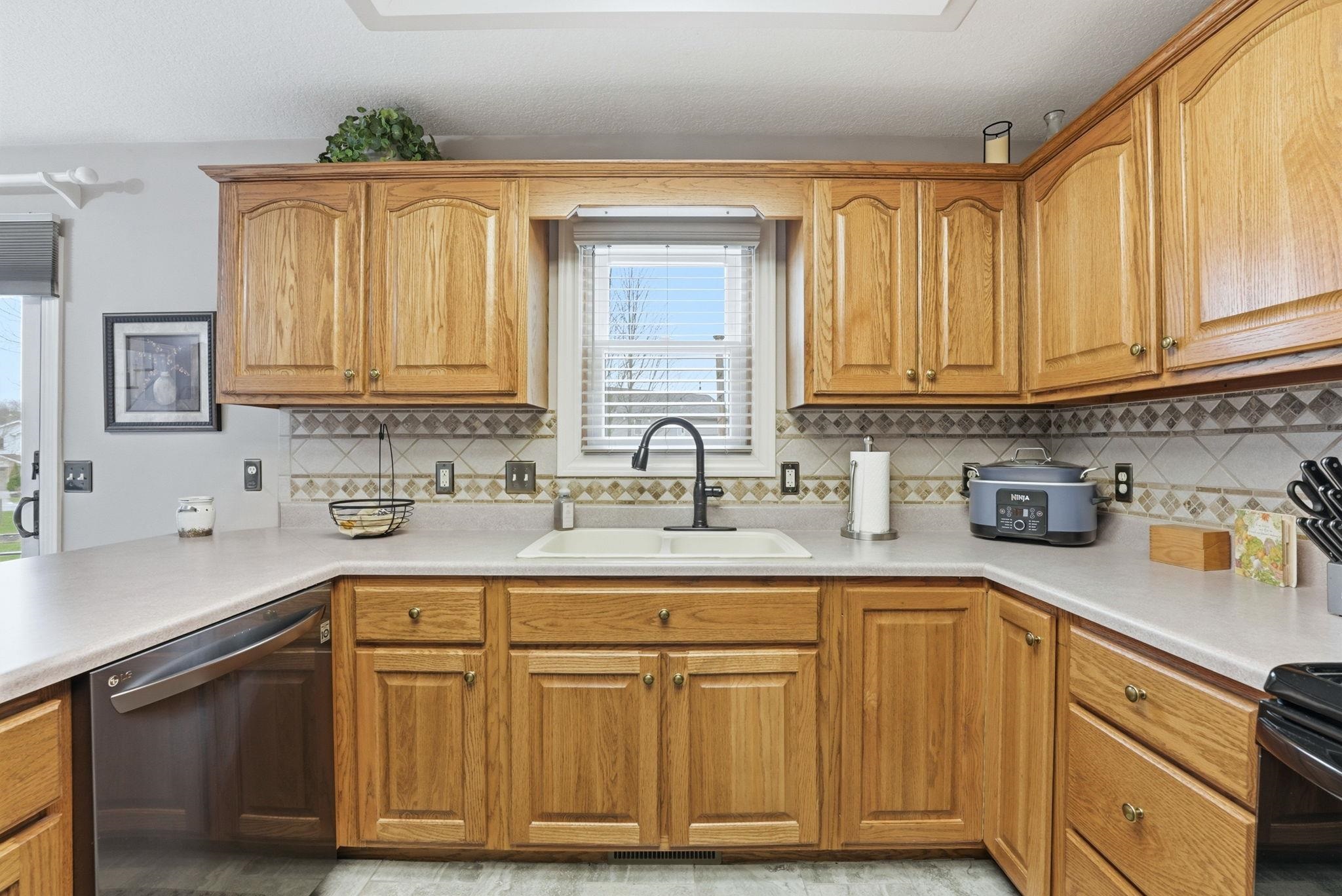 Kitchen featuring dishwasher, light countertops, wood finish cabinetry, and black range