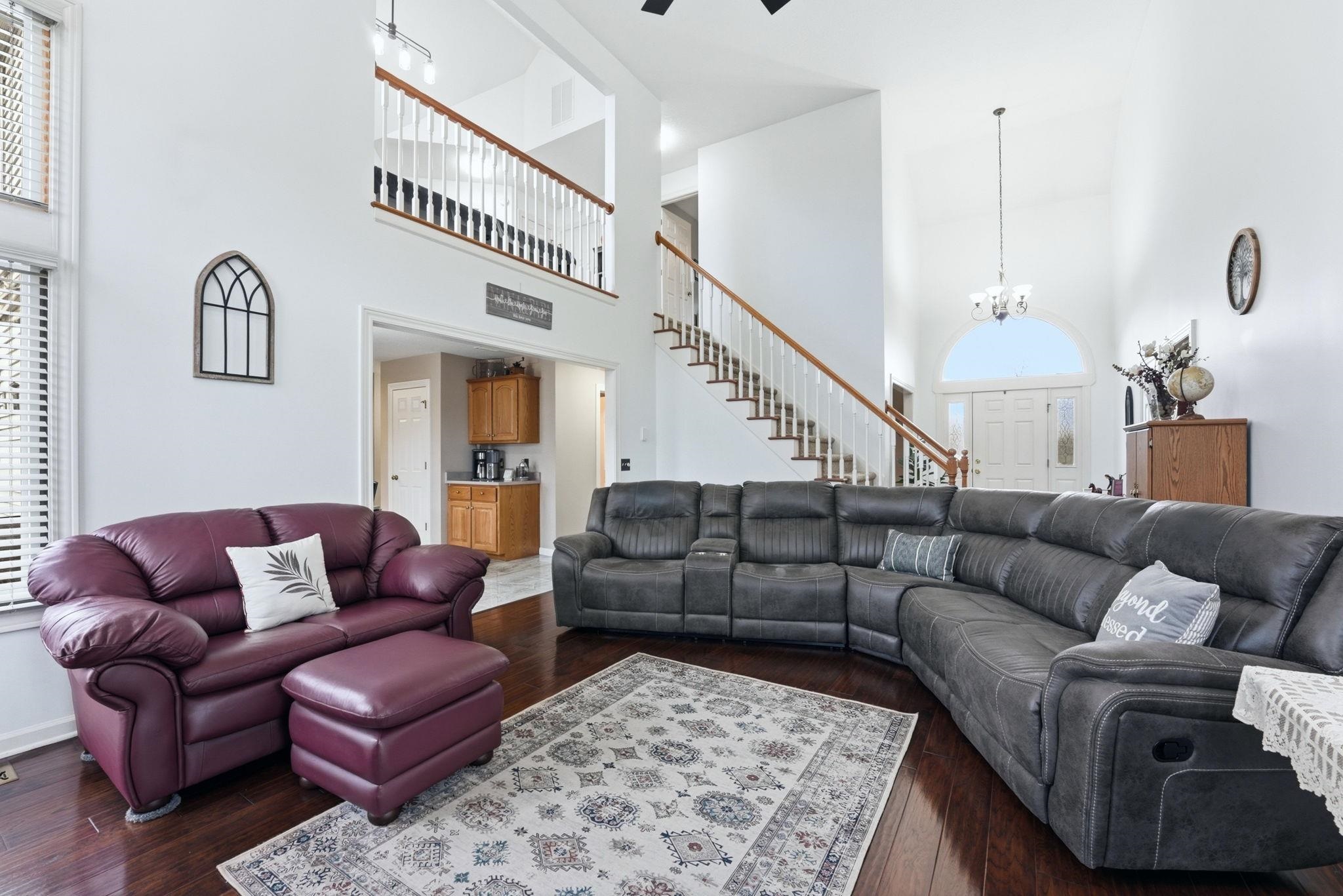 Living room featuring dark wood-style floors, a high ceiling, a chandelier, and a ceiling fan