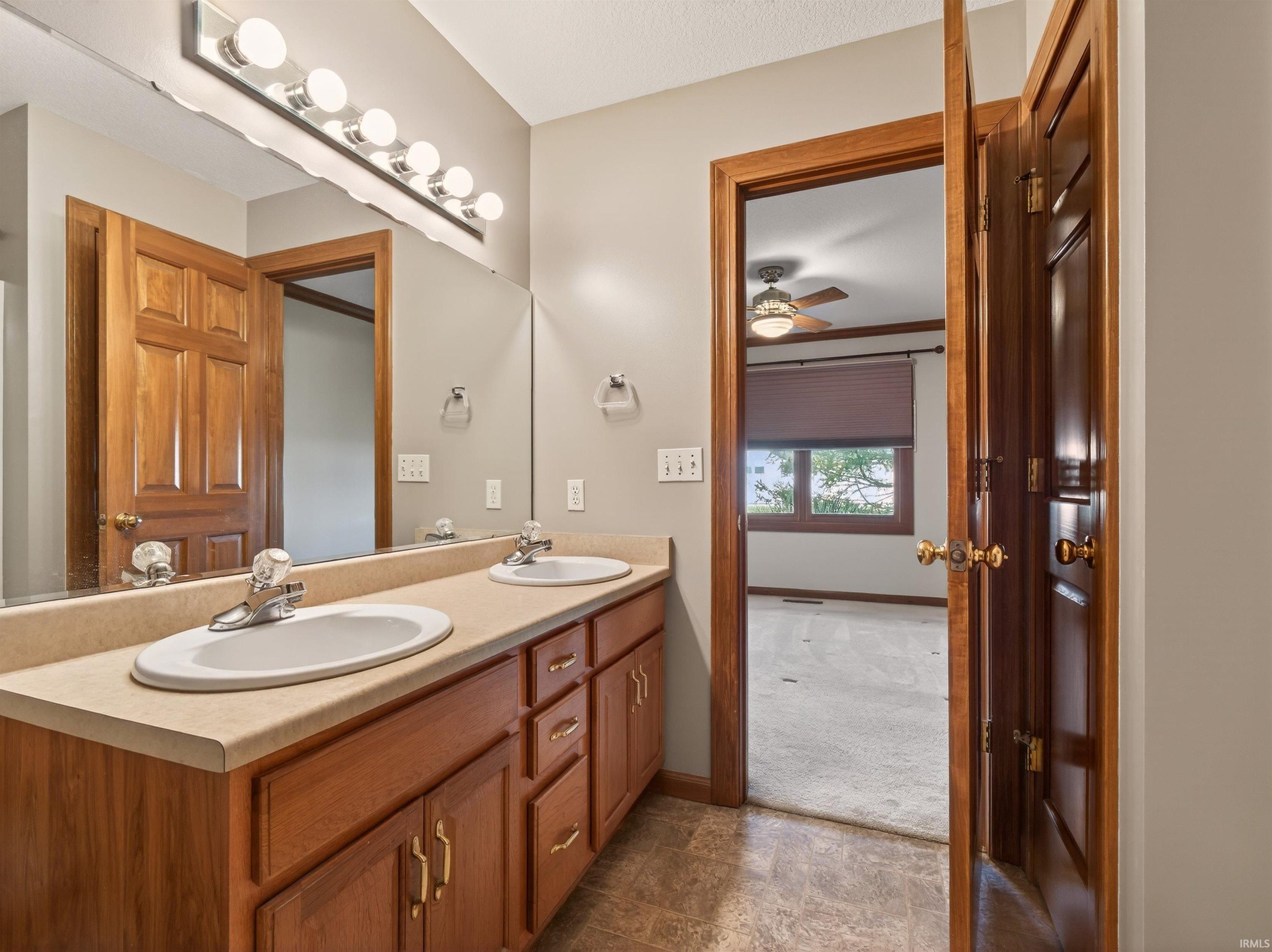 Bathroom with double vanity, ceiling fan, stone finish floors, and light colored carpet