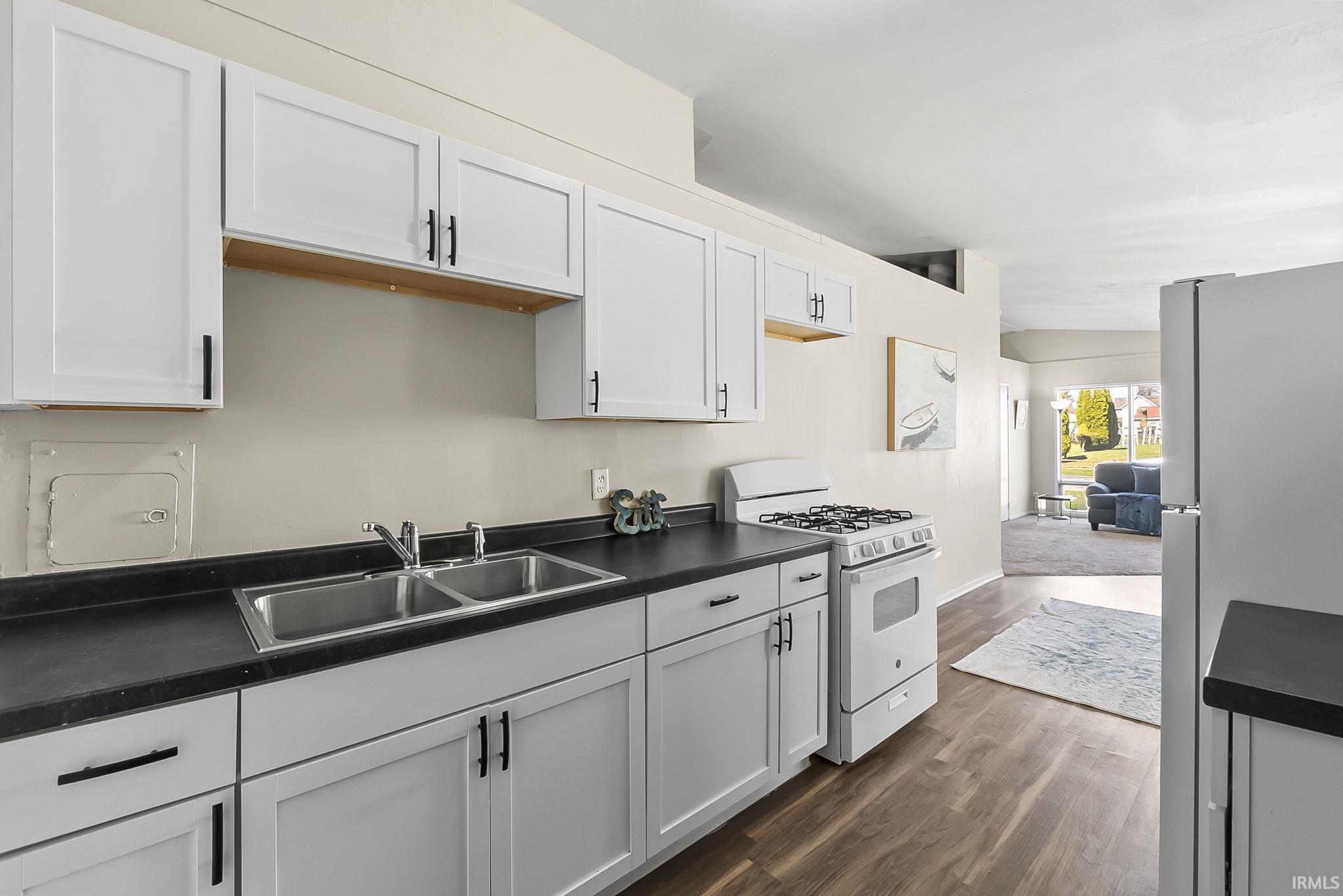 Kitchen with dark countertops, white gas stove, freestanding refrigerator, and dark wood-style floors