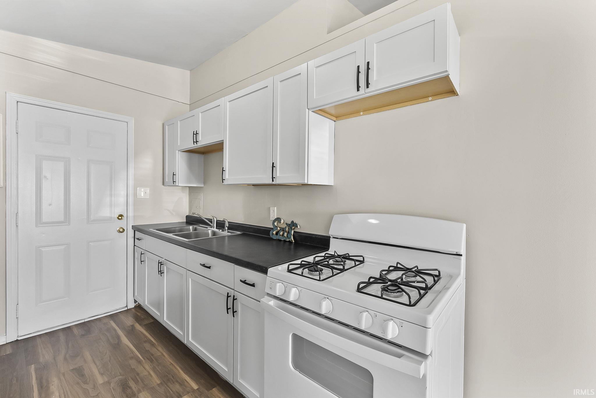 Kitchen with white gas range oven, dark wood-style floors, white cabinets, and dark countertops