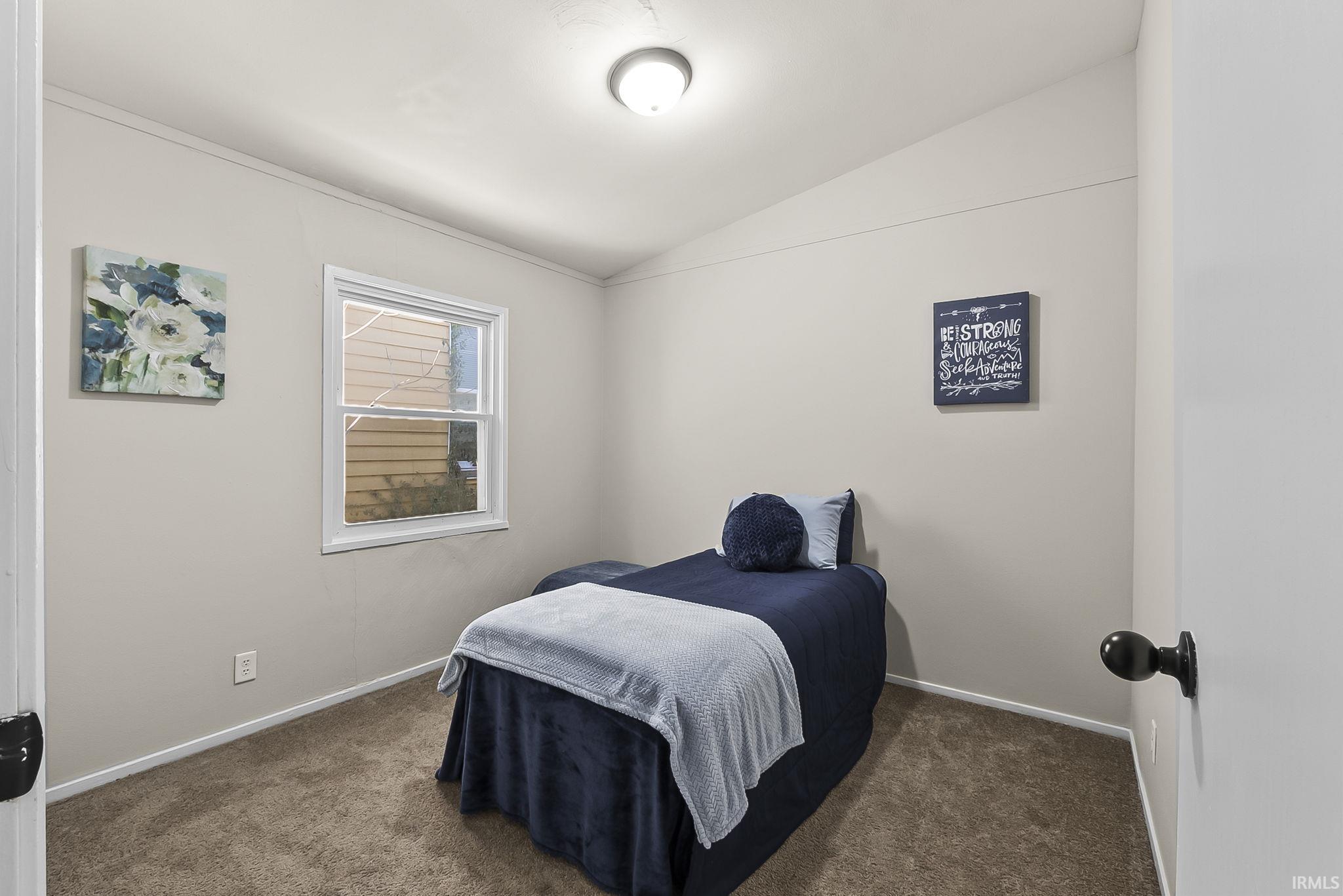Bedroom featuring lofted ceiling and dark carpet