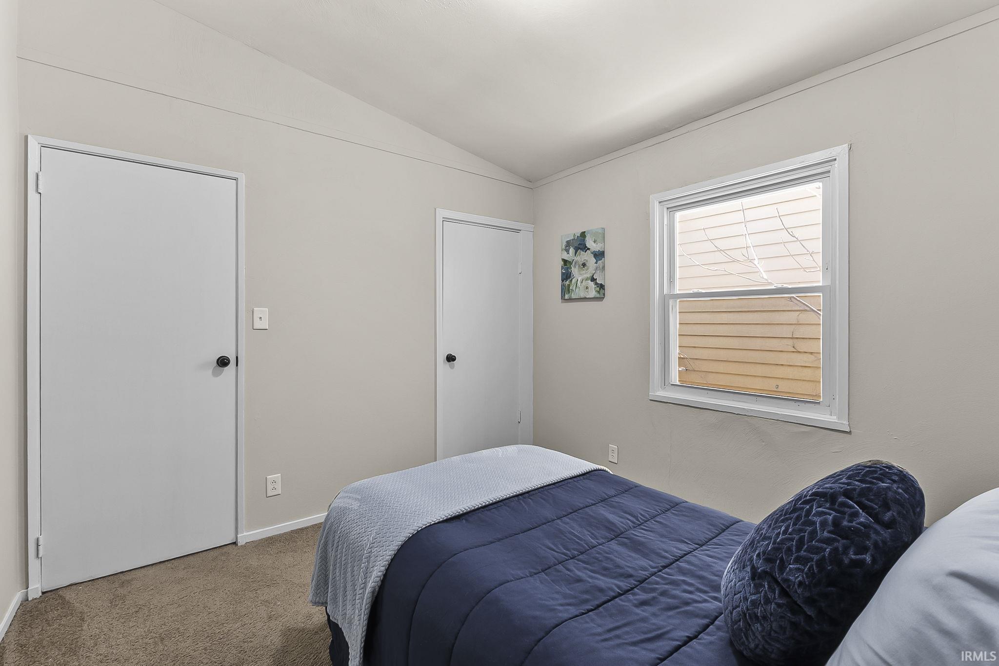 Carpeted bedroom with vaulted ceiling and baseboards