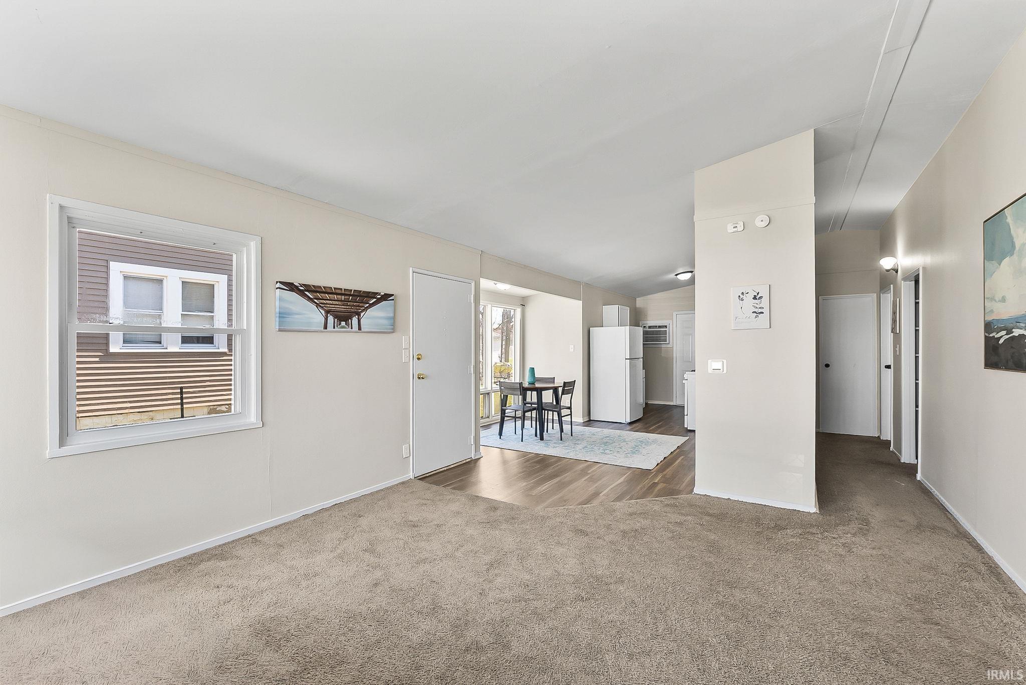 Unfurnished living room featuring lofted ceiling and dark colored carpet