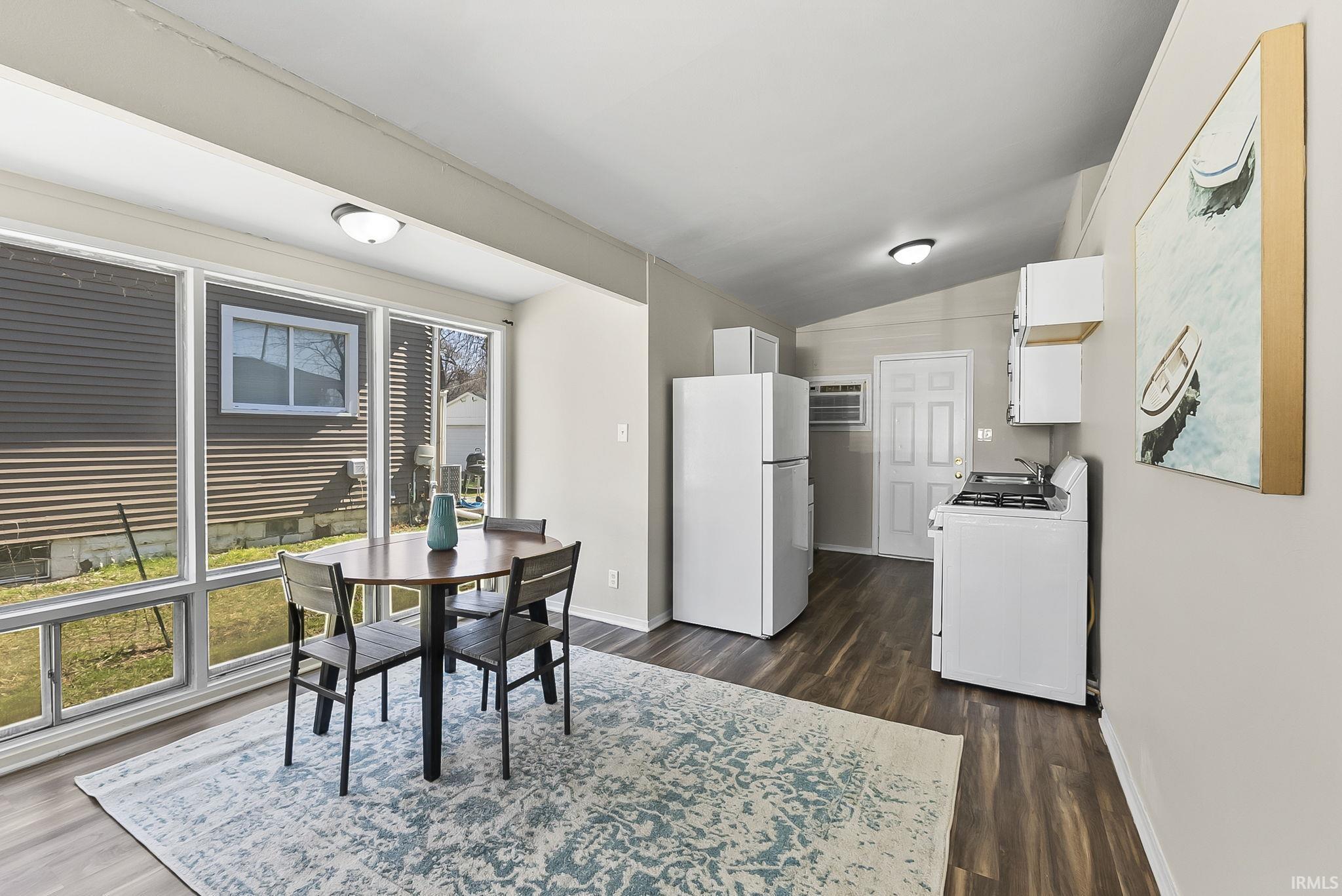 Dining space with vaulted ceiling and dark wood-style flooring