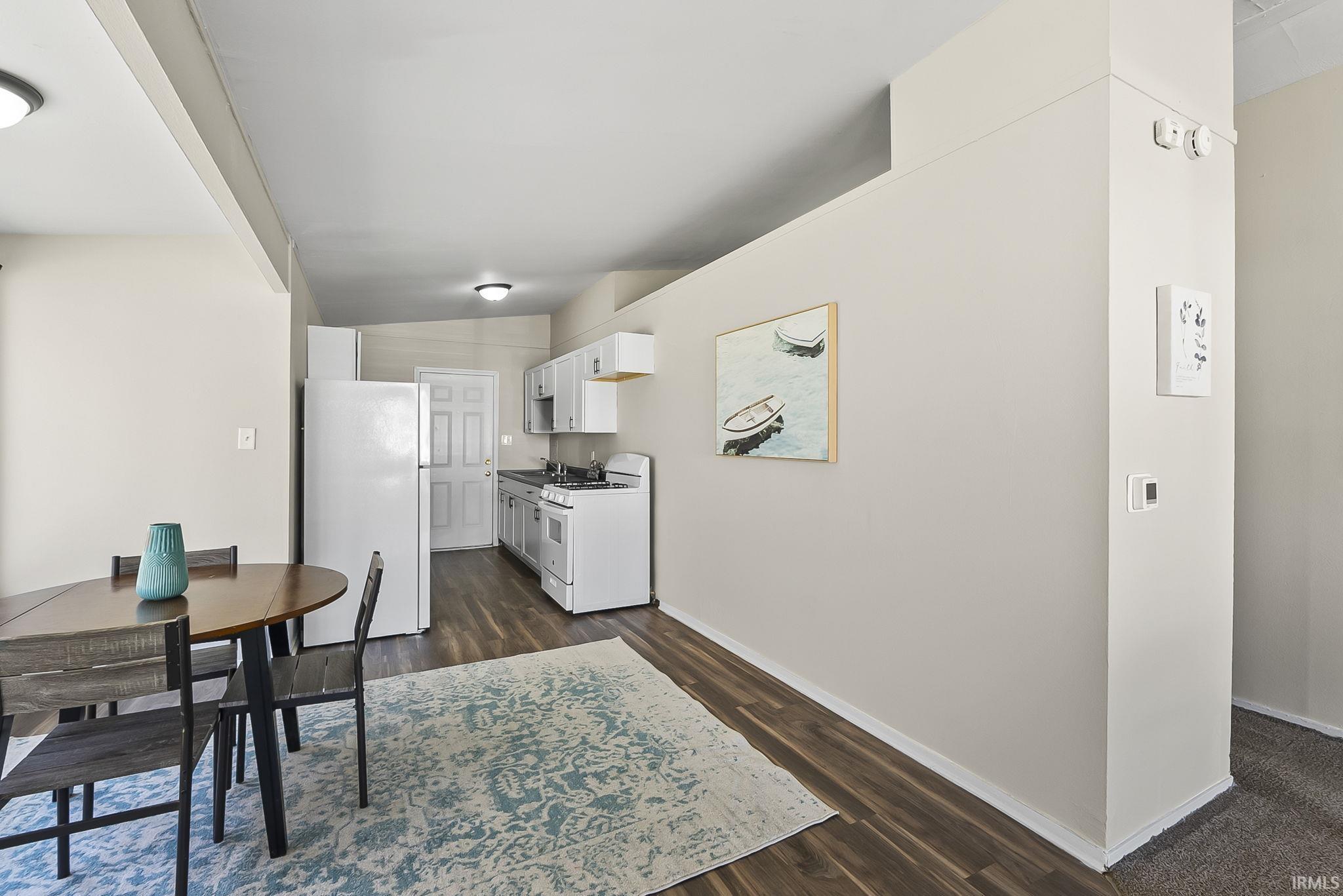 Kitchen featuring white appliances, white cabinetry, lofted ceiling, dark wood-type flooring, and light countertops