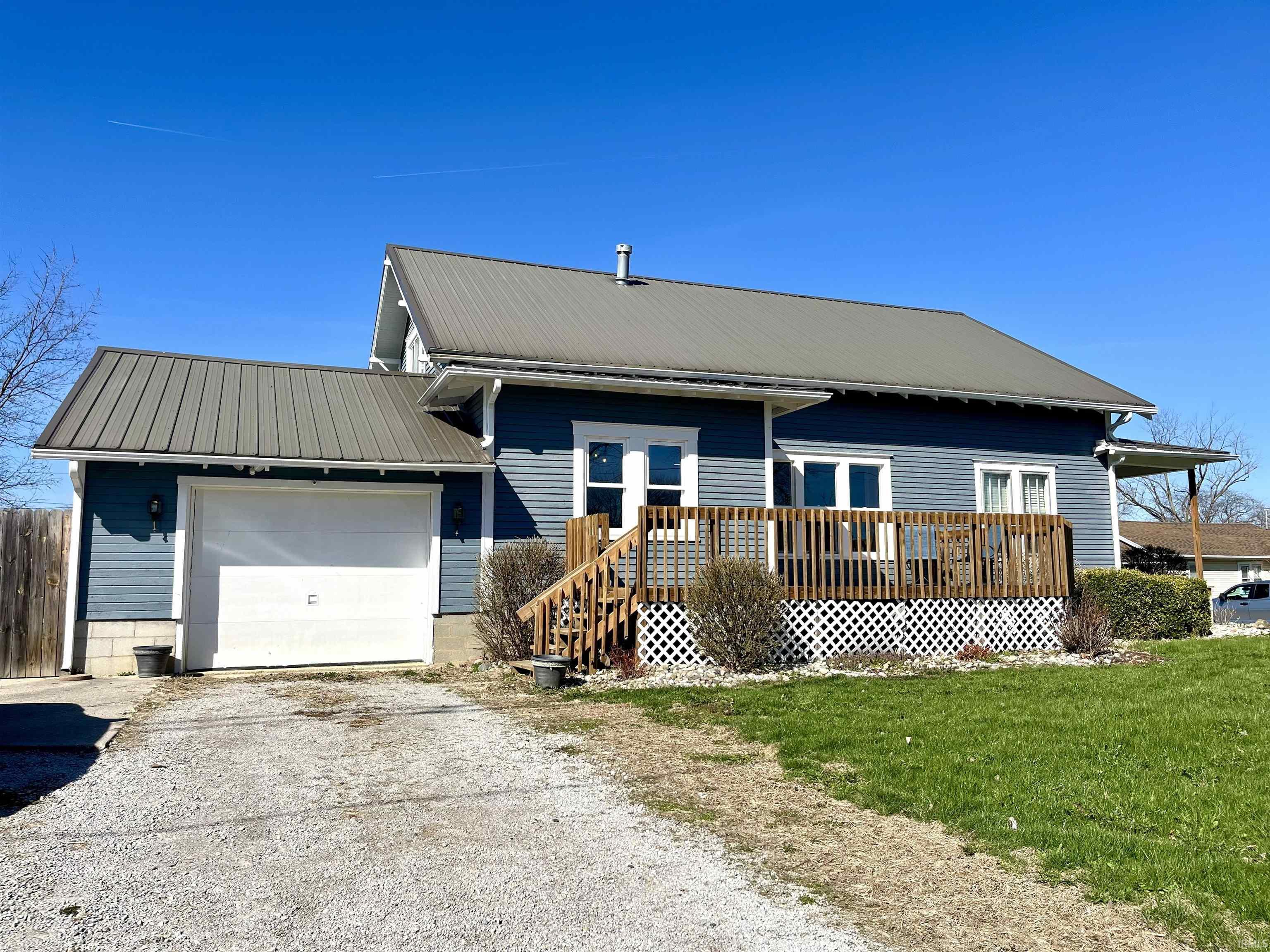 Single story home featuring a deck, an attached garage, concrete driveway, and a metal roof