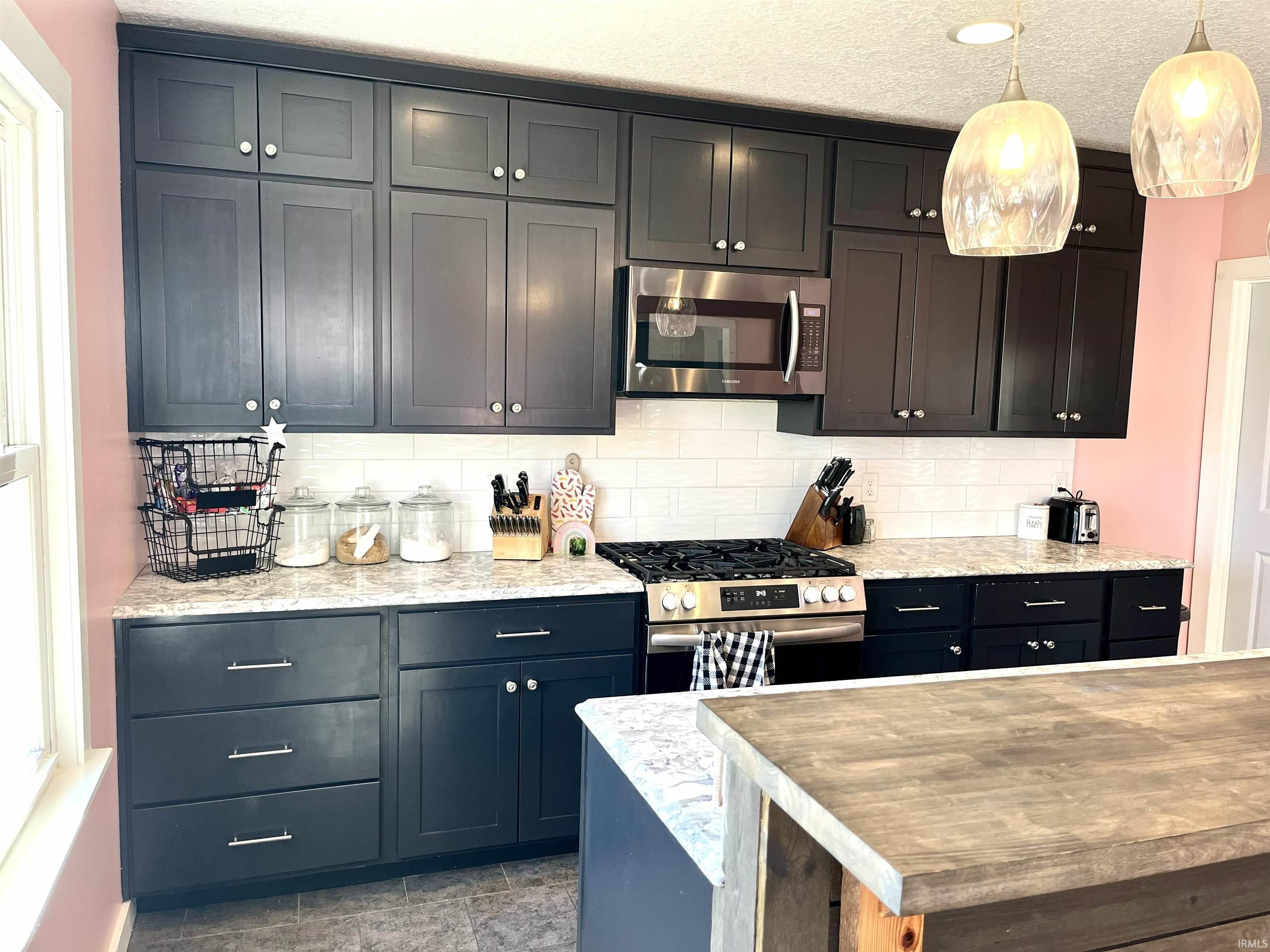 Kitchen with stainless steel appliances, decorative backsplash, a textured ceiling, hanging light fixtures, and a kitchen island