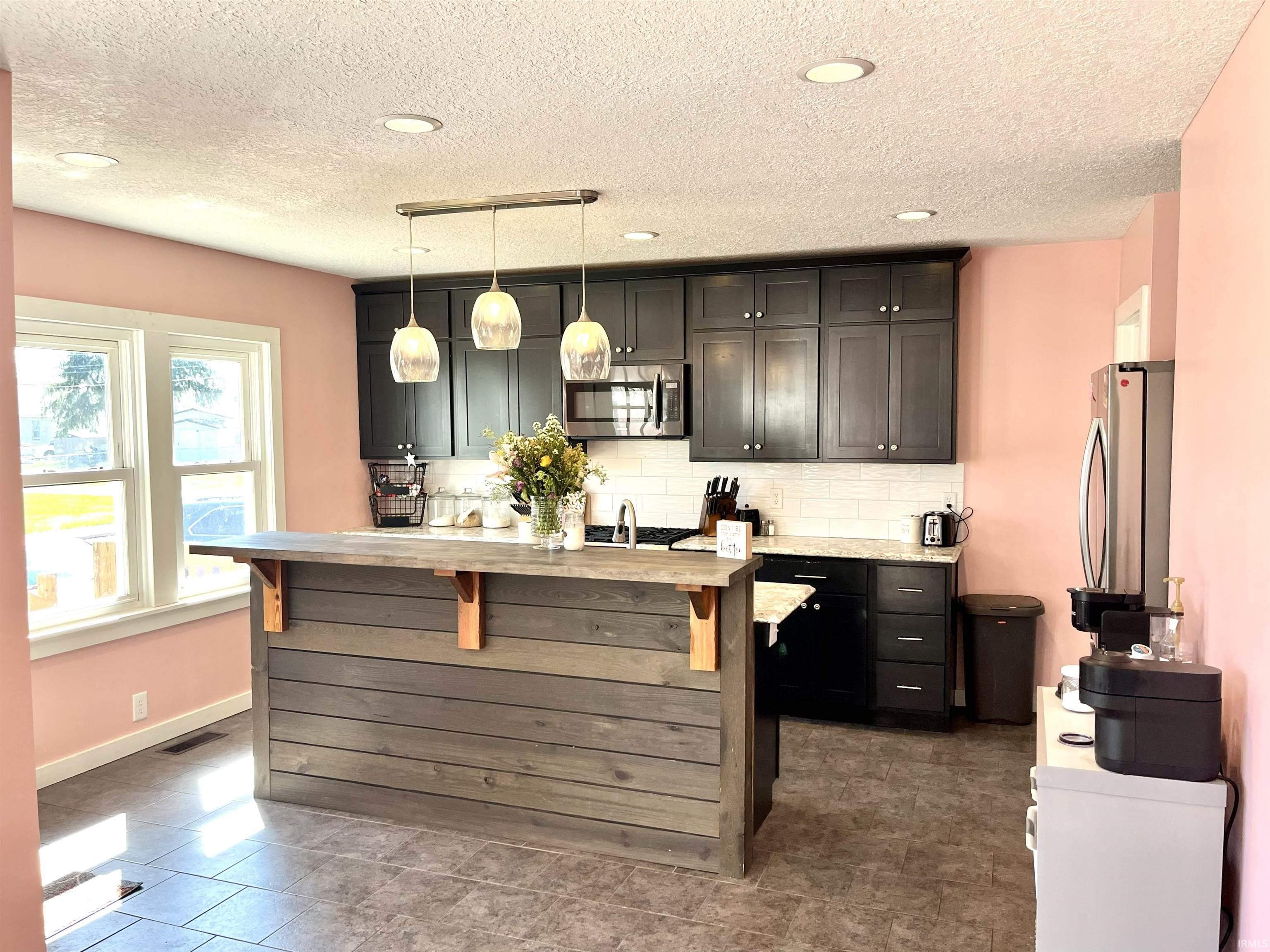 Kitchen with tasteful backsplash, stainless steel appliances, a kitchen bar, light stone counters, and hanging light fixtures
