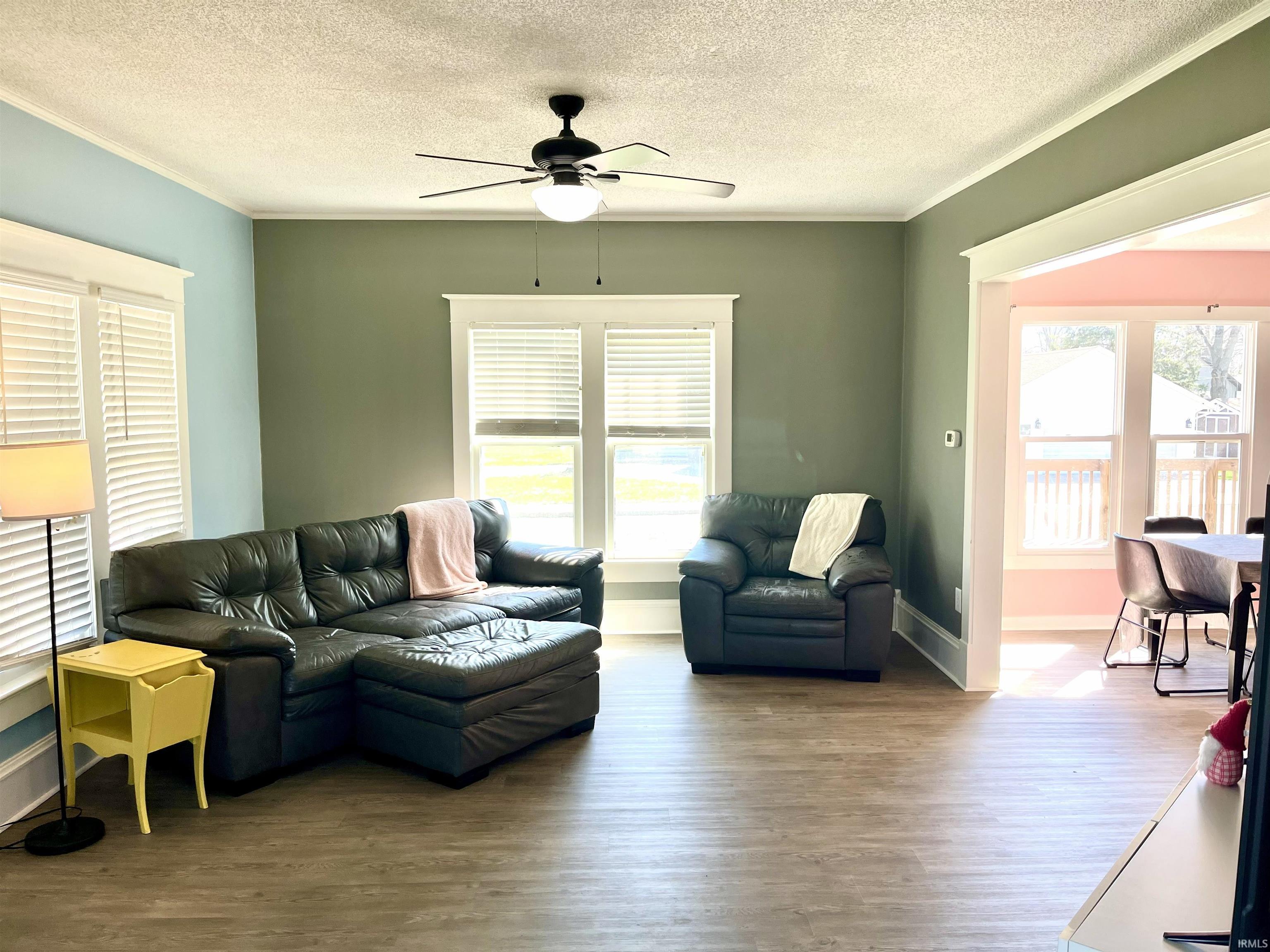 Living area with ceiling fan, wood finished floors, a textured ceiling, and crown molding