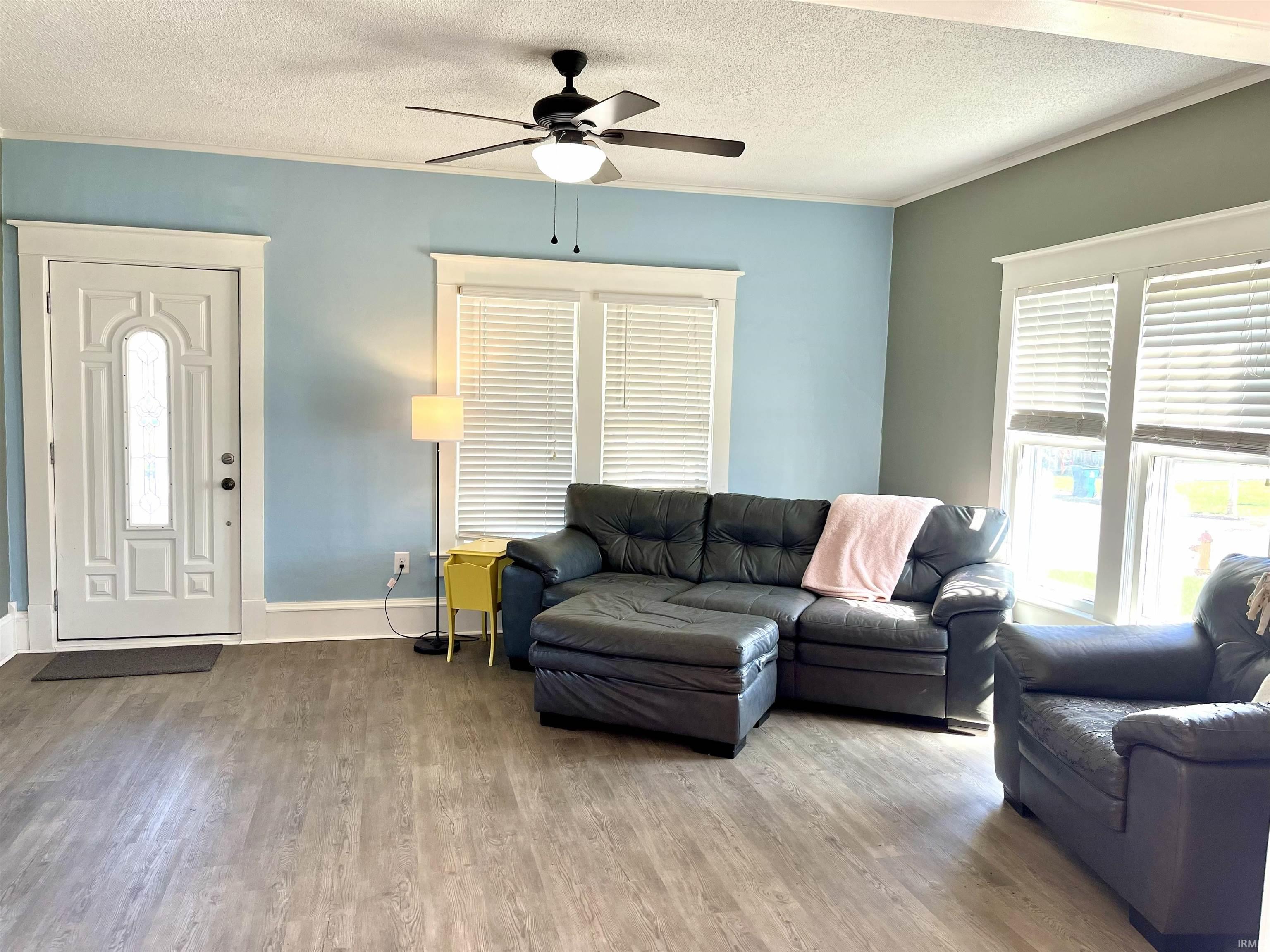 Living area with a textured ceiling, wood finished floors, a ceiling fan, and ornamental molding