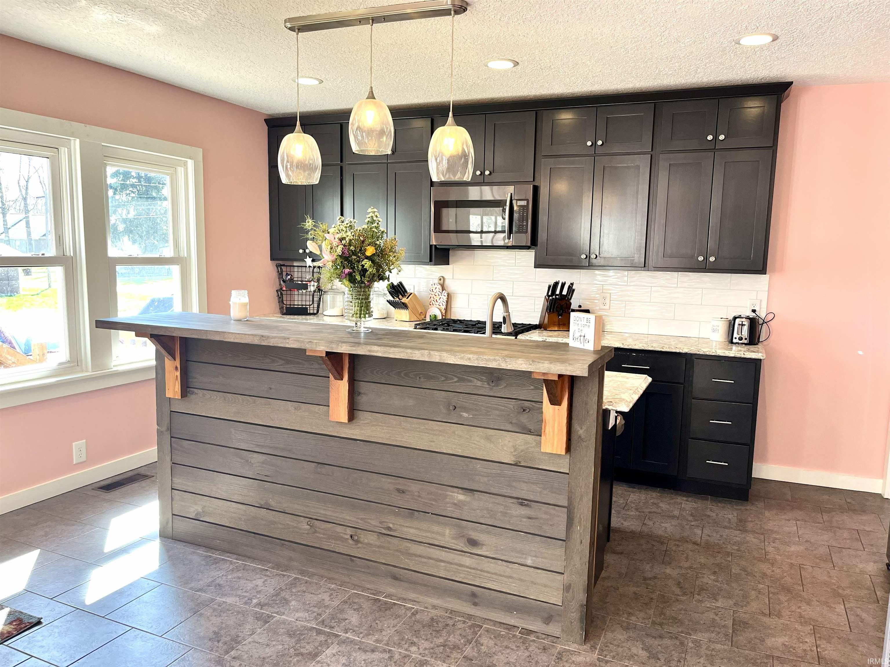 Kitchen featuring stainless steel microwave, tasteful backsplash, hanging light fixtures, a textured ceiling, and light stone counters