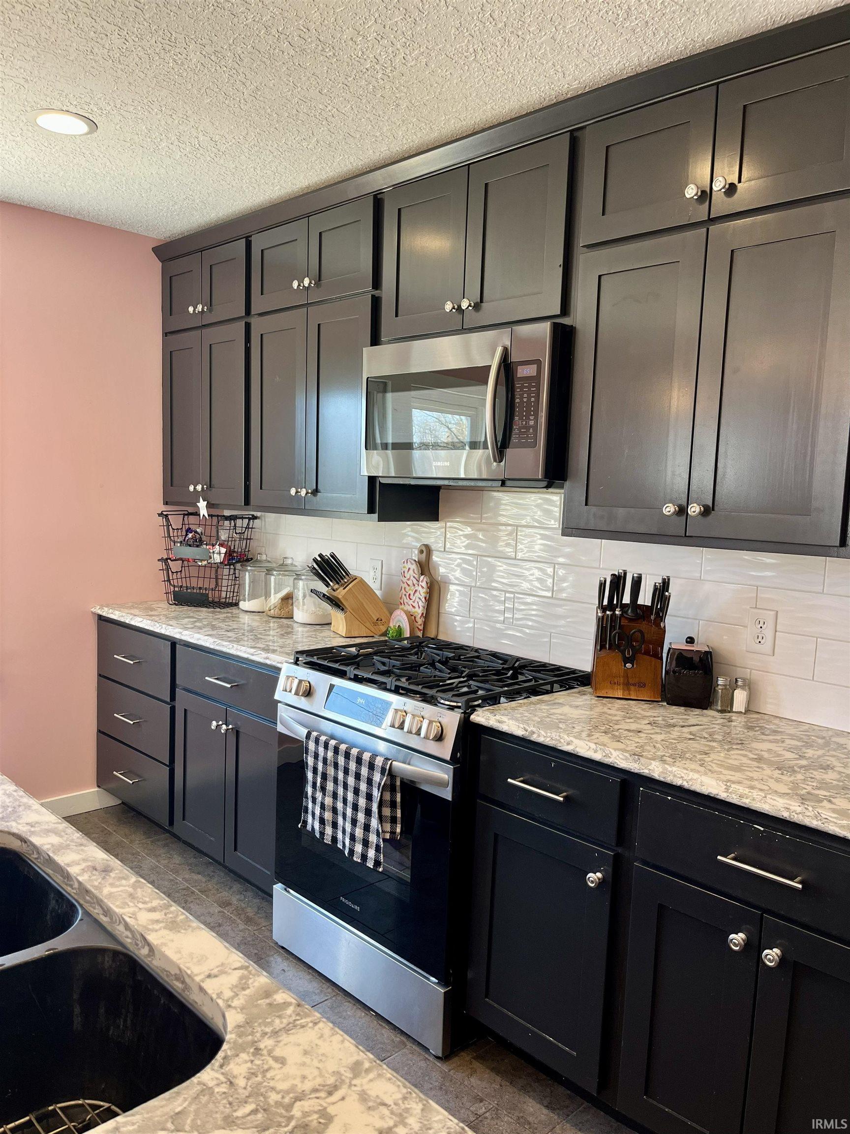 Kitchen with stainless steel appliances, tasteful backsplash, light stone counters, and a textured ceiling