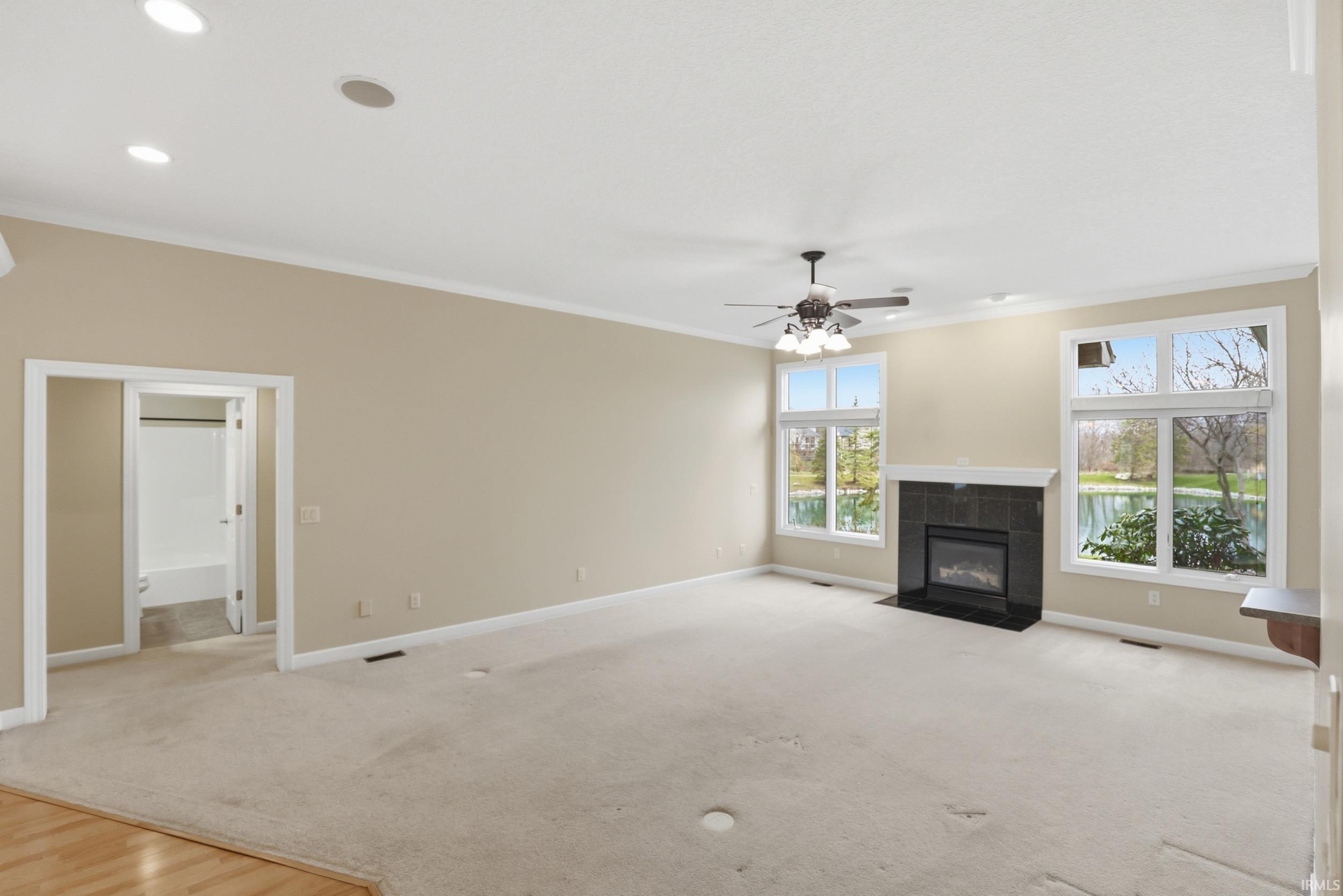 Unfurnished living room featuring a tile fireplace, ornamental molding, light carpet, and ceiling fan