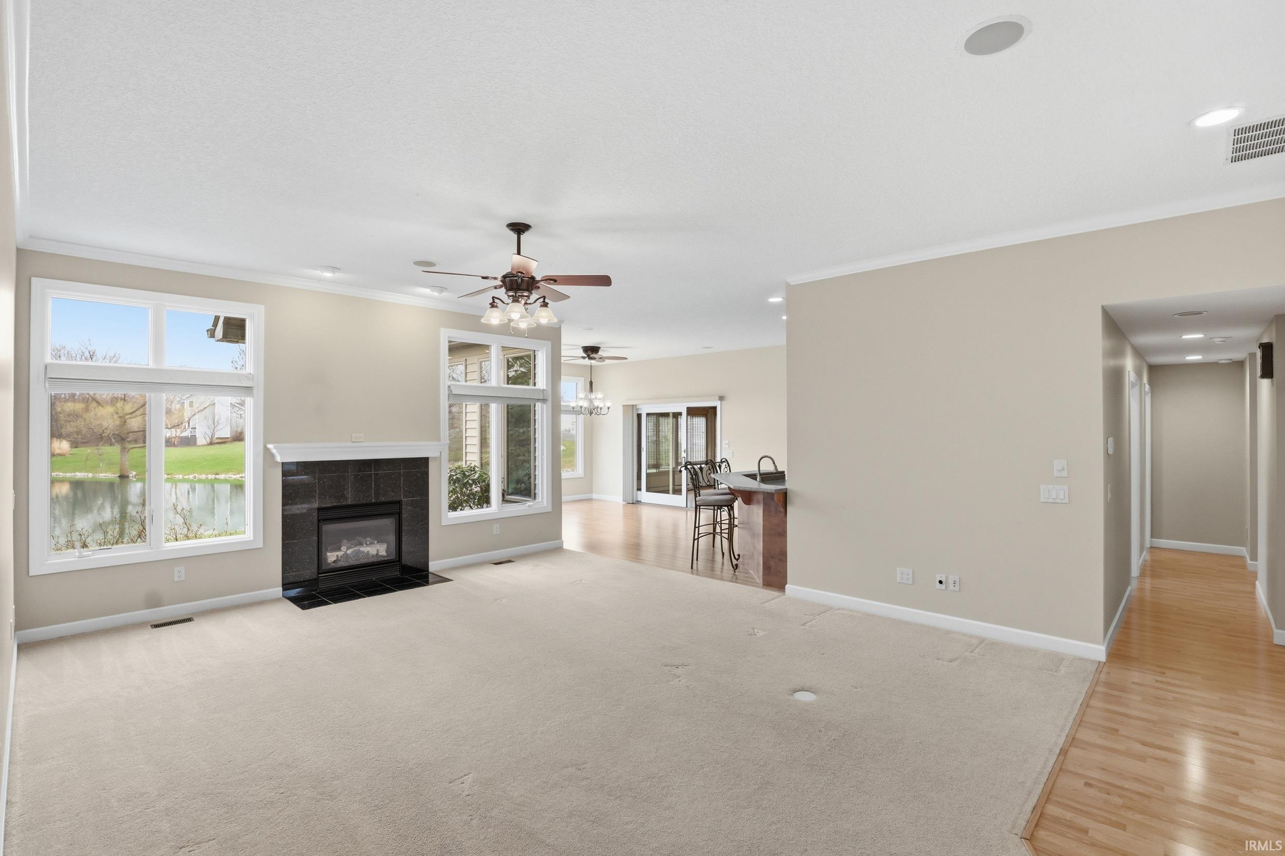 Living room with a tiled fireplace, ceiling fan, crown molding, healthy amount of natural light, and light colored carpet
