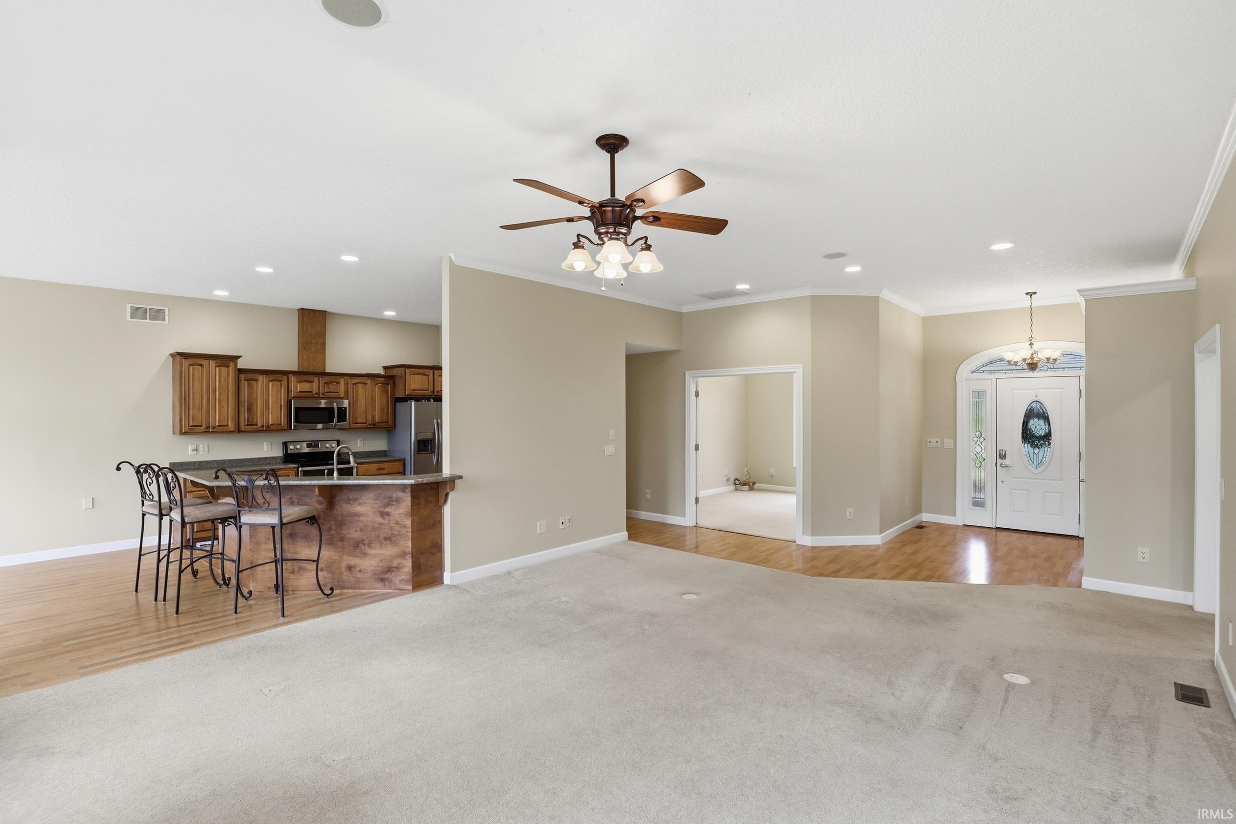 Living area featuring light colored carpet, a ceiling fan, crown molding, light wood finished floors, and suspended lighting