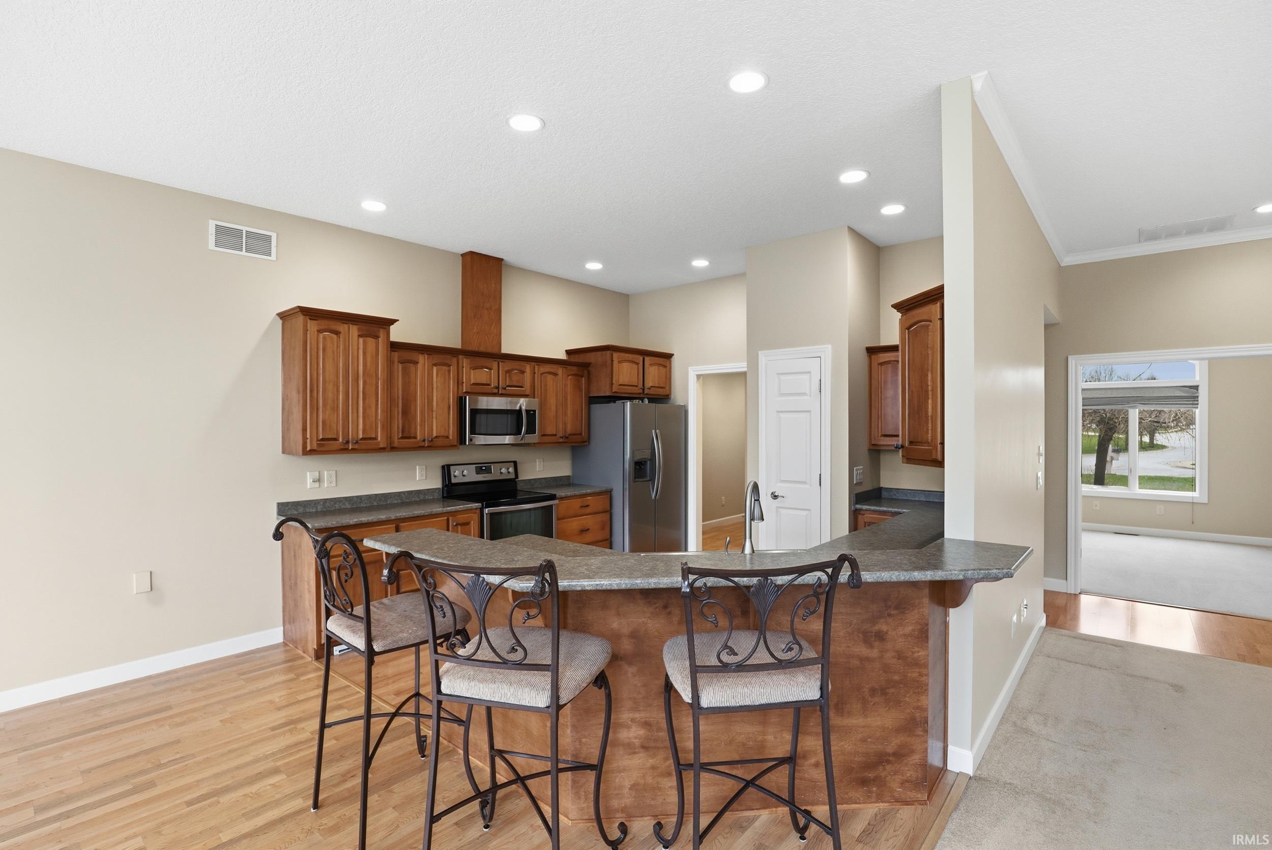 Kitchen with a kitchen breakfast bar, wood finish cabinetry, stainless steel appliances, light wood-style floors, and crown molding