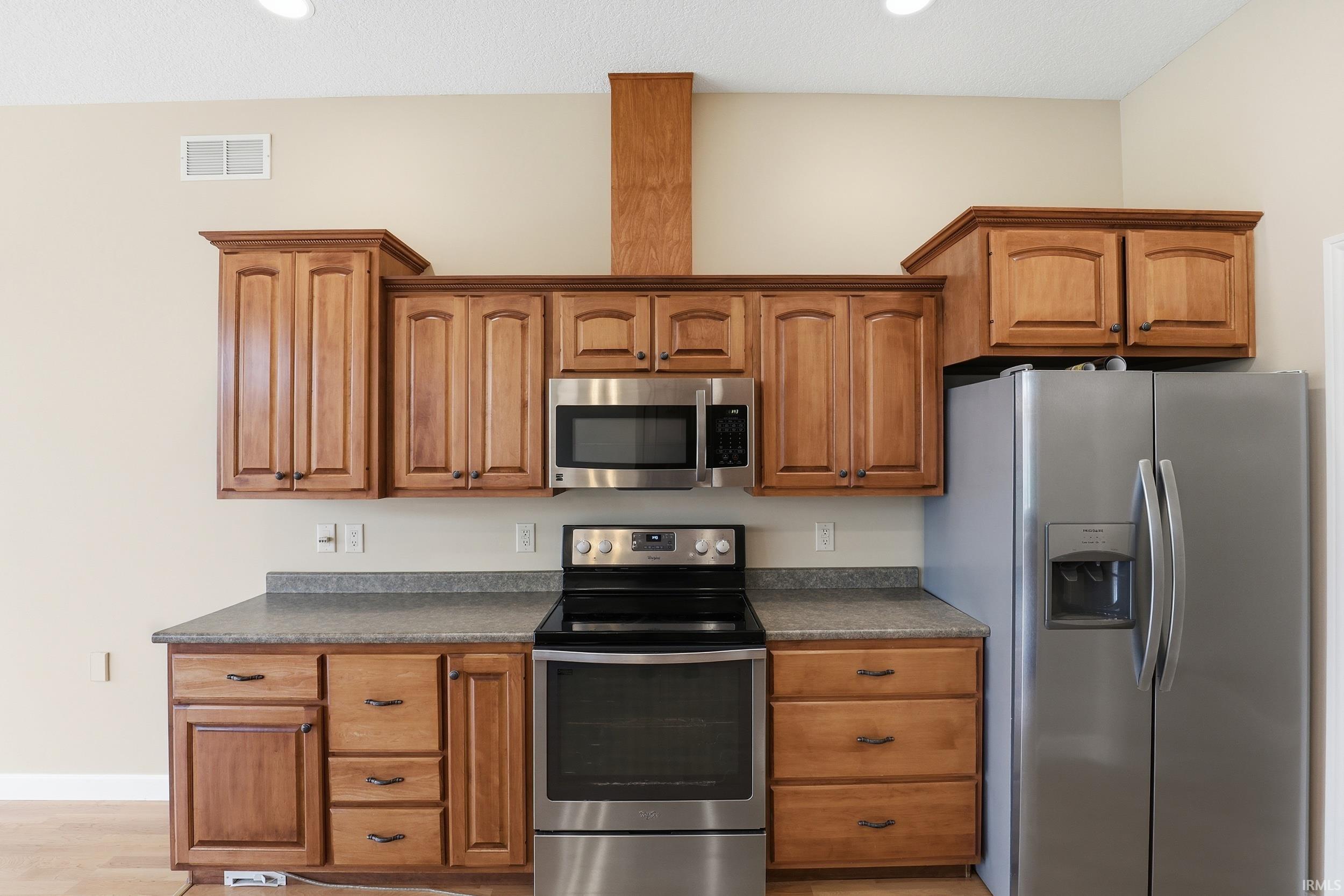 Kitchen featuring stainless steel appliances, dark countertops, wood finish cabinets, and recessed lighting