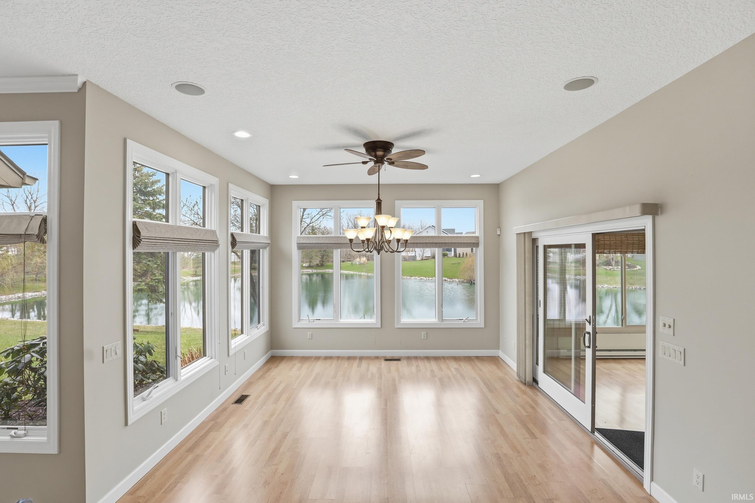 Unfurnished sunroom featuring wood finished floors, a water view, suspended lighting, and a textured ceiling